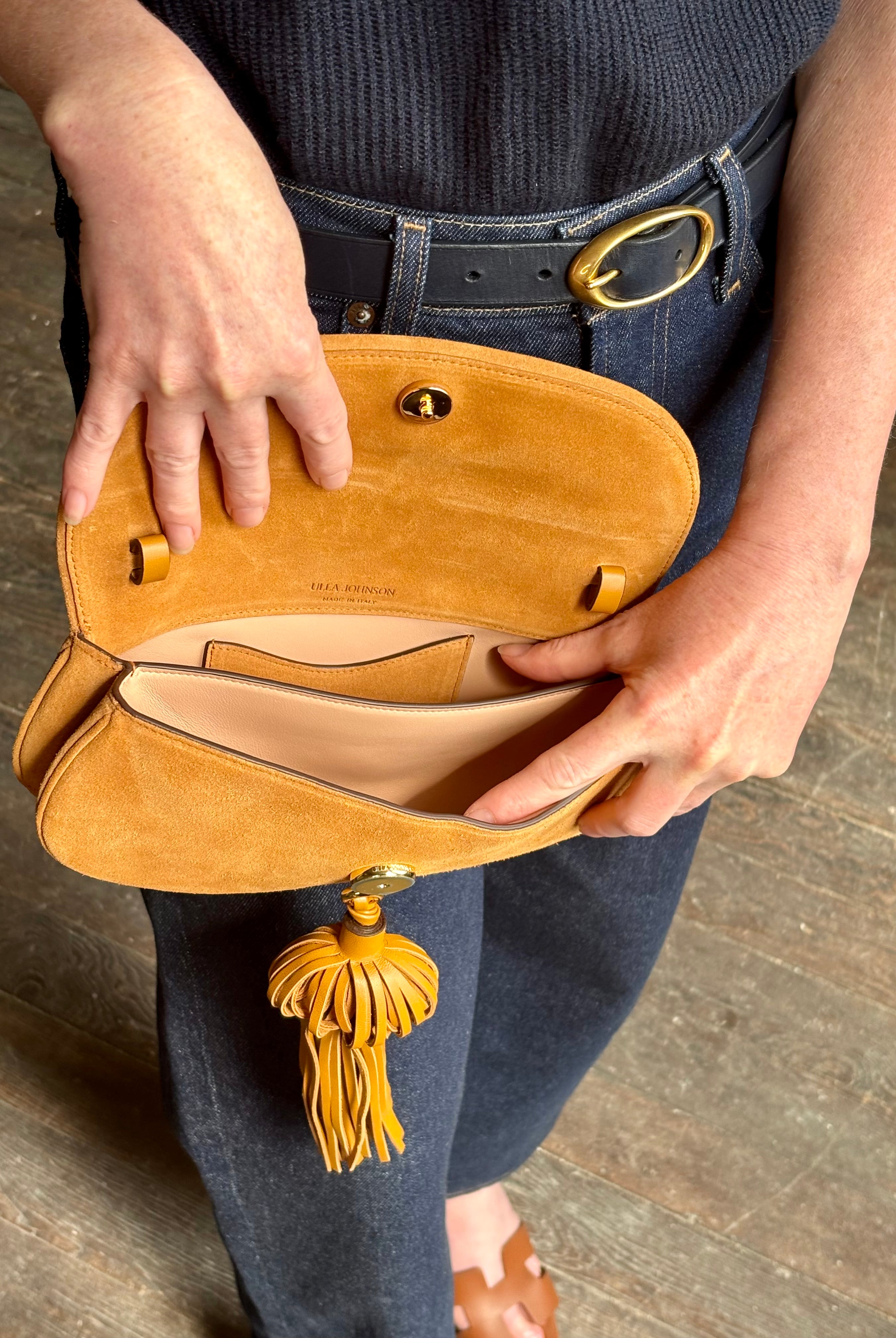 Mature woman with the luxury Italian leather Paloma handbag with Tassel Flap from Ulla Johnson rendered in a rich caramel brown featuring a pull tassel magnetic snap closure and removable adjustable handle that seamlessly converts to a designer clutch