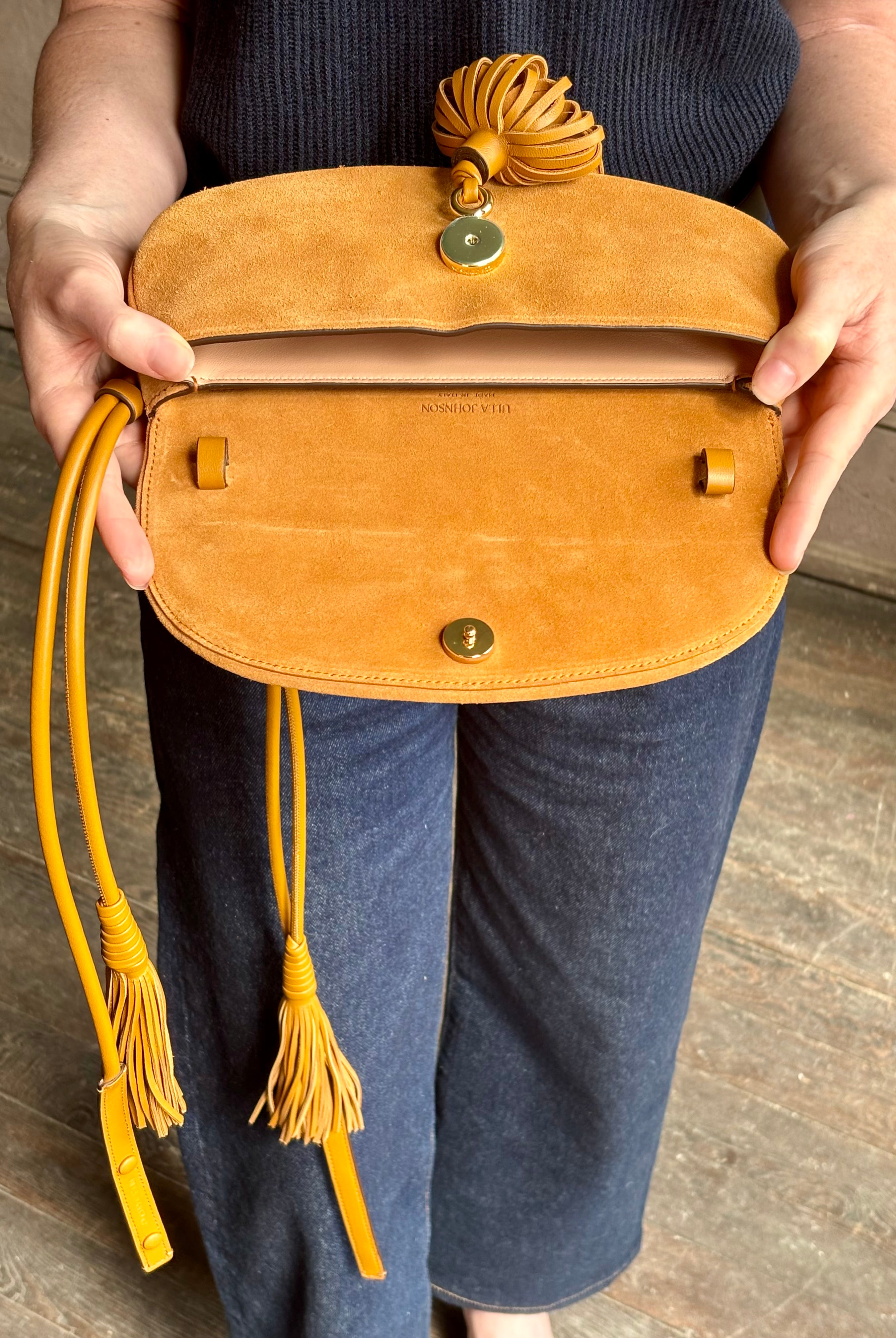 Mature woman with the luxury Italian leather Paloma handbag with Tassel Flap from Ulla Johnson rendered in a rich caramel brown featuring a pull tassel magnetic snap closure and removable adjustable handle that seamlessly converts to a designer clutch