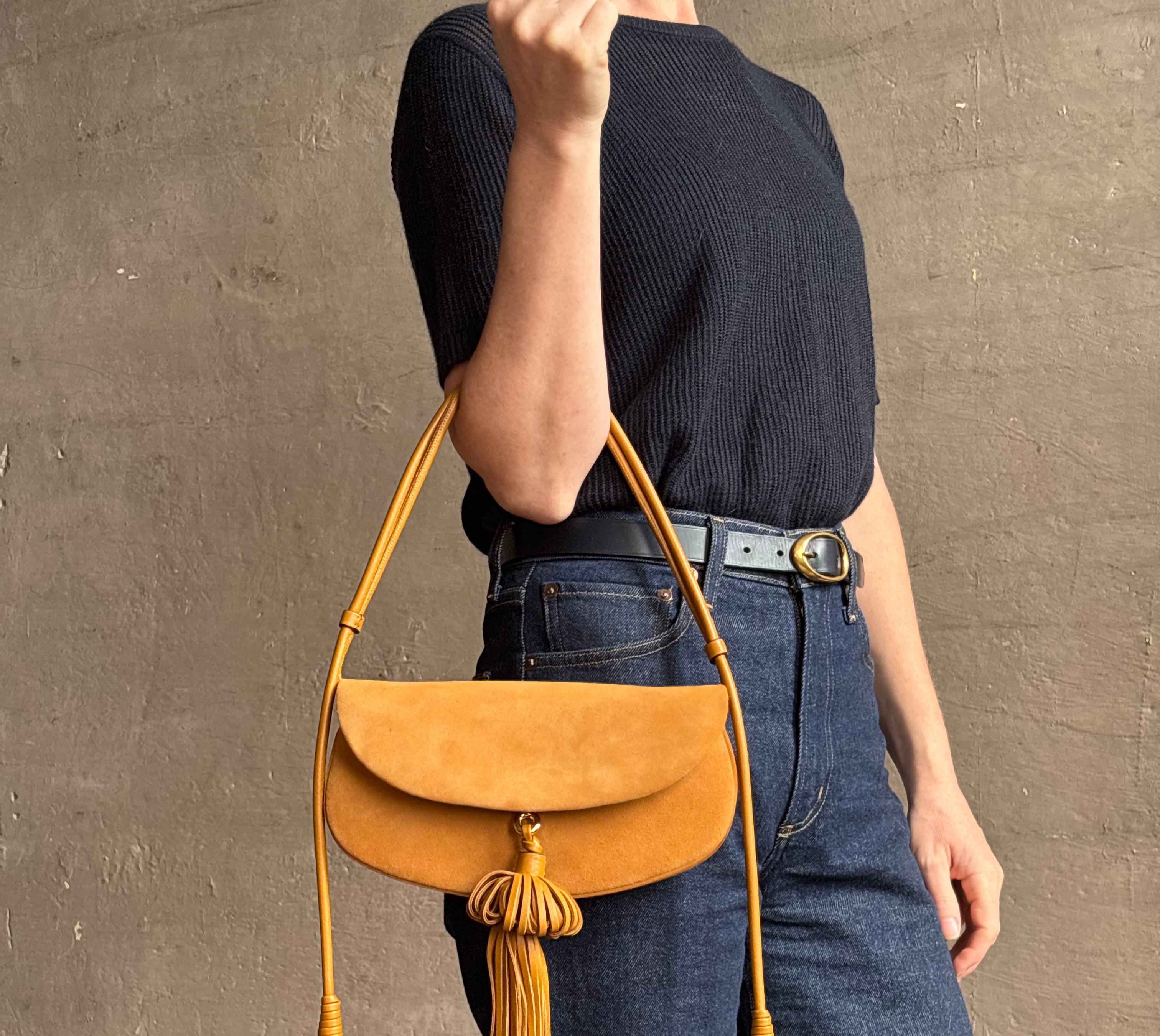 Mature woman with the luxury Italian leather Paloma handbag with Tassel Flap from Ulla Johnson rendered in a rich caramel brown featuring a pull tassel magnetic snap closure and removable adjustable handle that seamlessly converts to a designer clutch