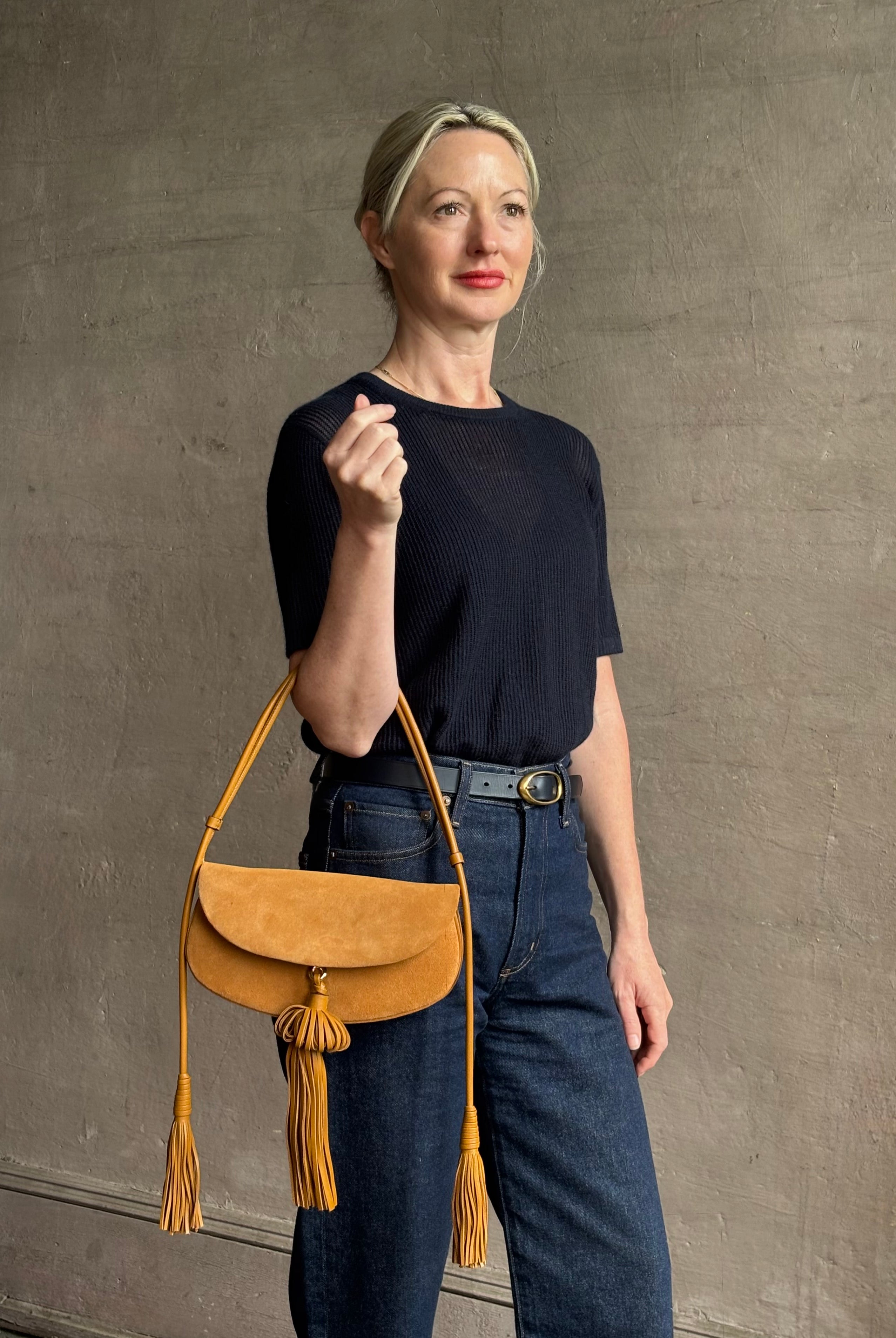 Mature woman with the luxury Italian leather Paloma handbag with Tassel Flap from Ulla Johnson rendered in a rich caramel brown featuring a pull tassel magnetic snap closure and removable adjustable handle that seamlessly converts to a designer clutch