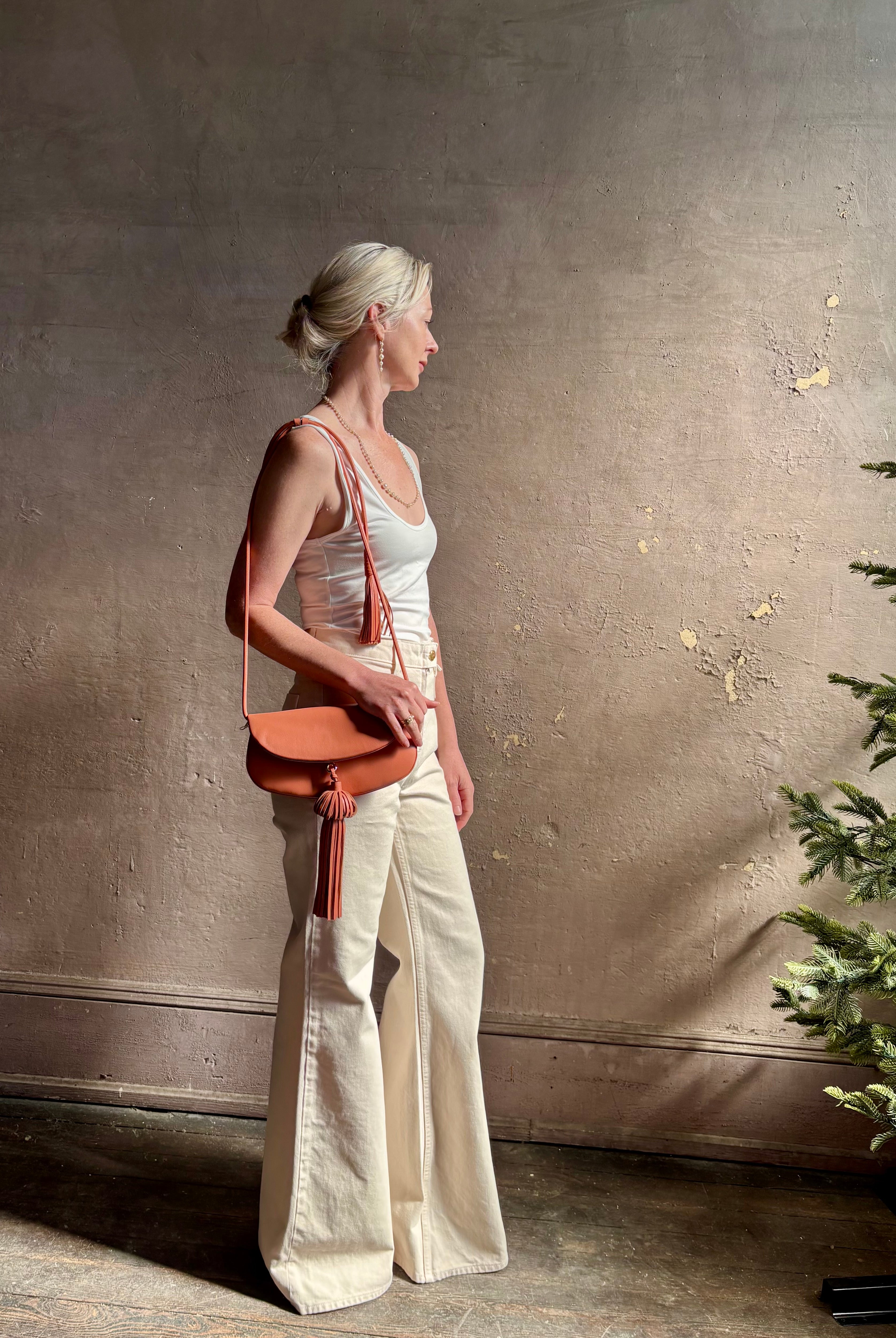 Mature woman with the luxury Italian leather Paloma handbag with Tassel Flap from Ulla Johnson rendered in a warm pink featuring a pull tassel magnetic snap closure and removable adjustable handle that seamlessly converts to a designer clutch