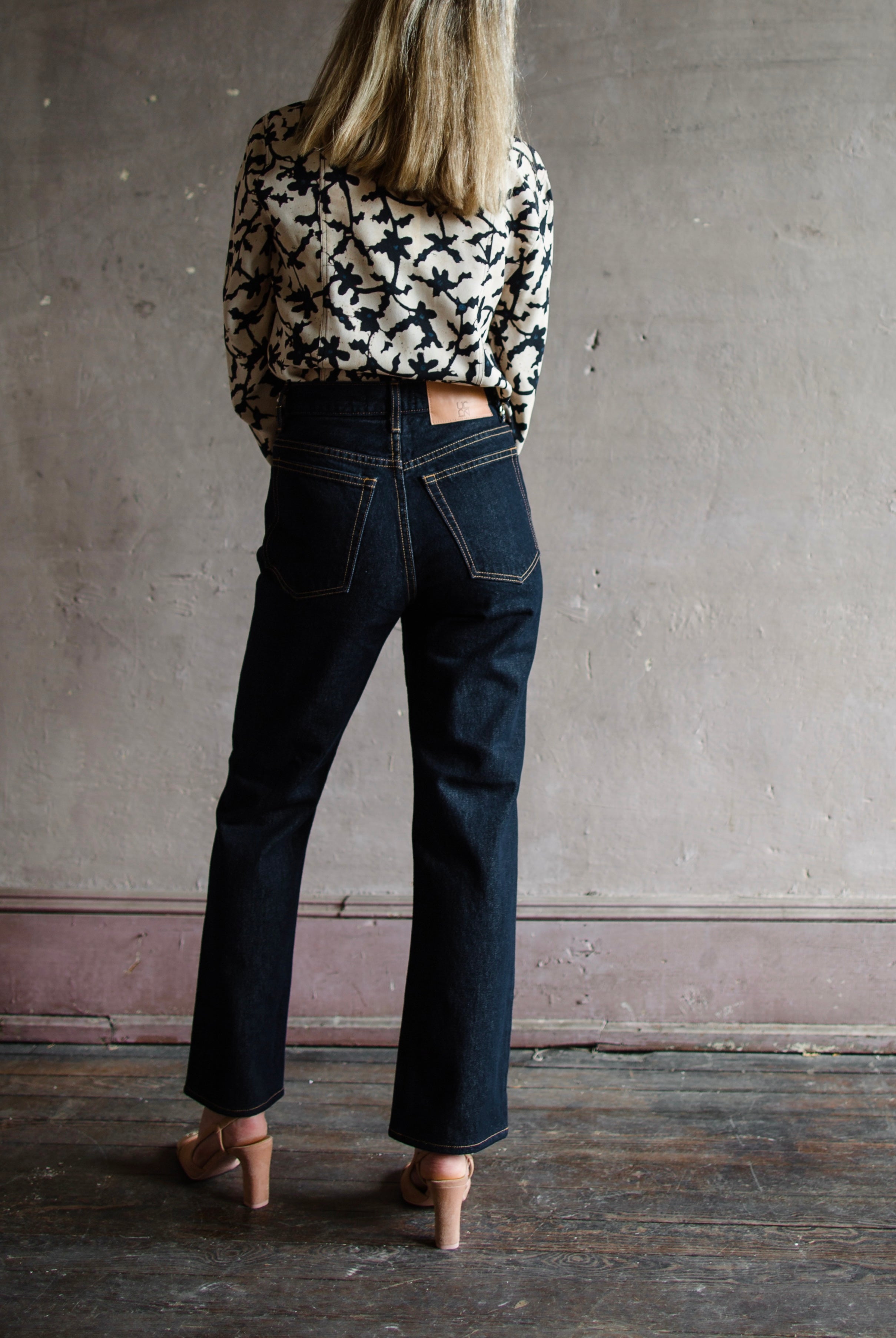 Mature model wearing designer denim jean by Ulla Johnson with a  high rise straight, cropped leg with contrast stitching in dark wash.