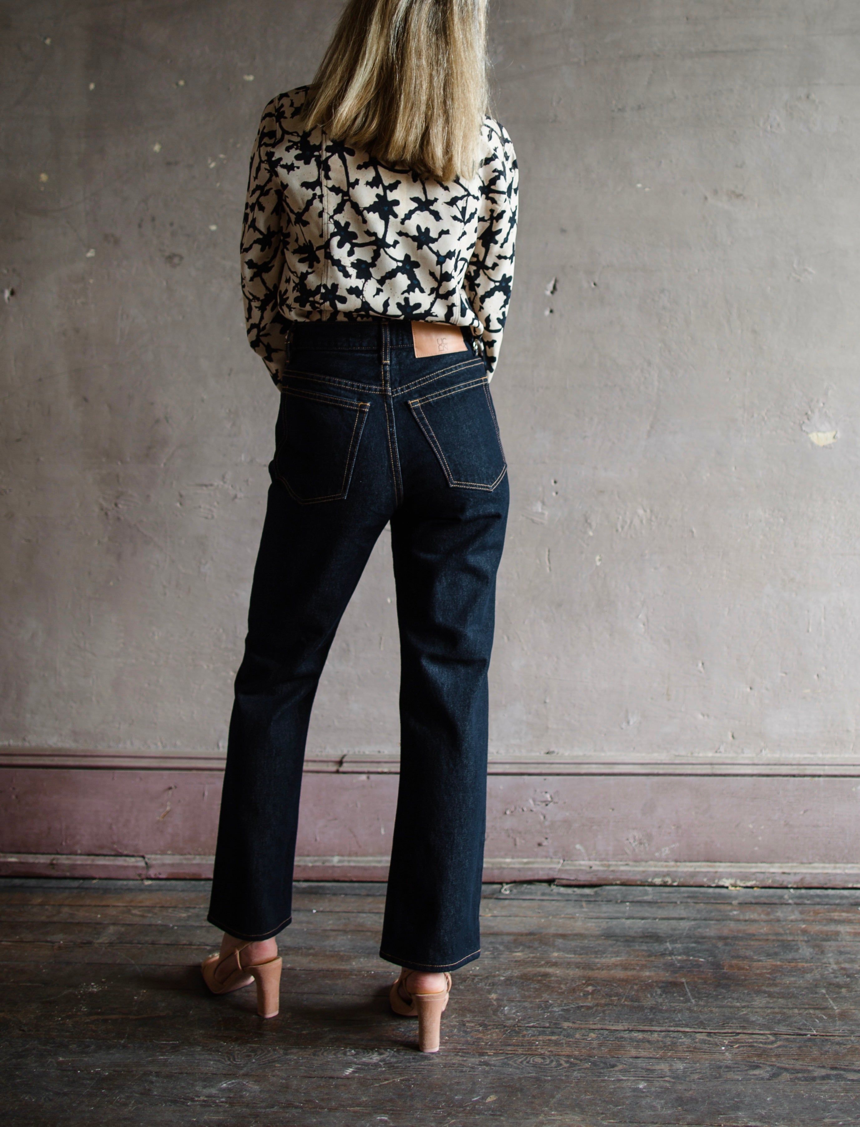 Mature model wearing designer denim jean by Ulla Johnson with a  high rise straight, cropped leg with contrast stitching in dark wash.
