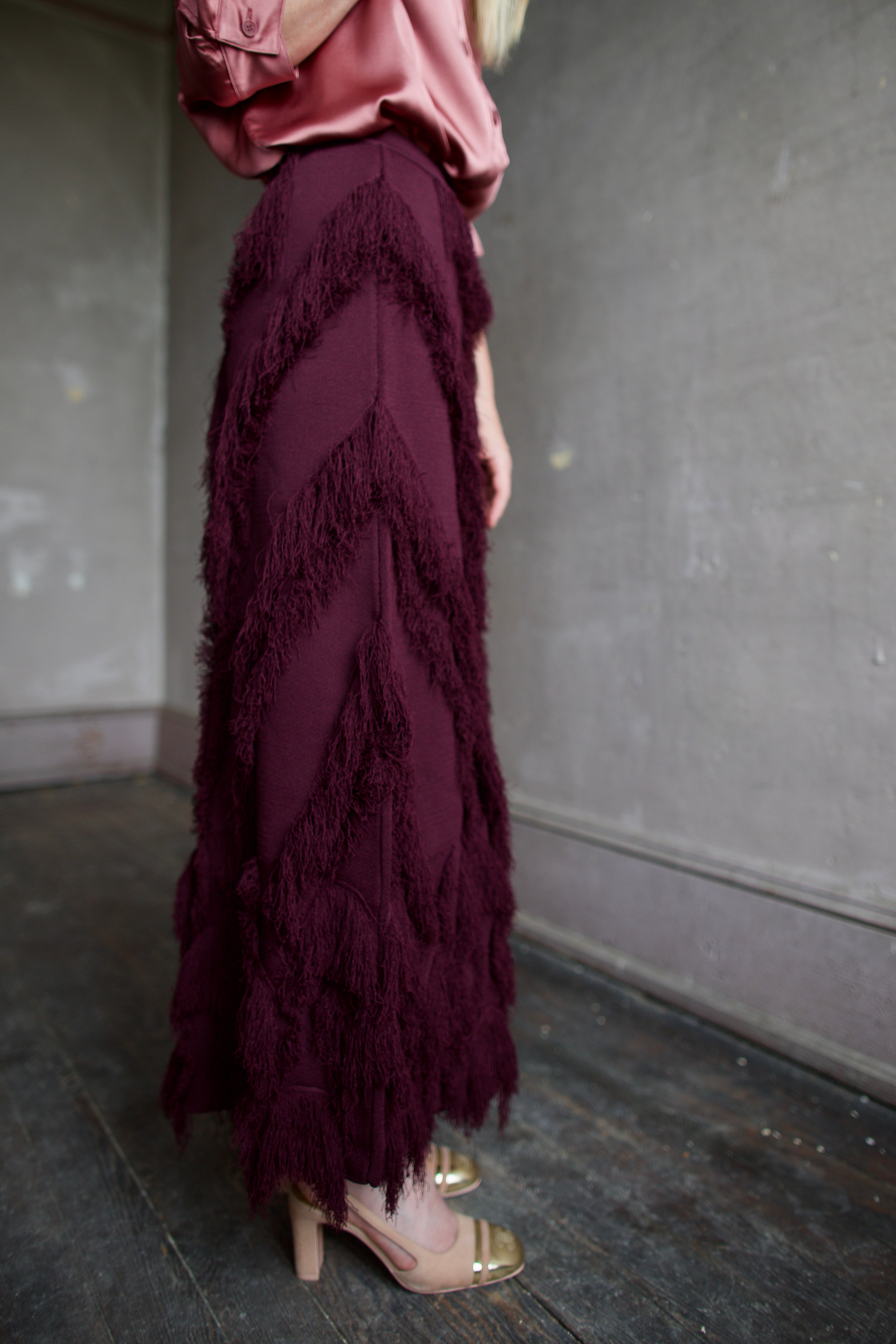 Mature model wearing a long burgundy skirt with a playful textured fringe pattern that can easily be dressed up or down