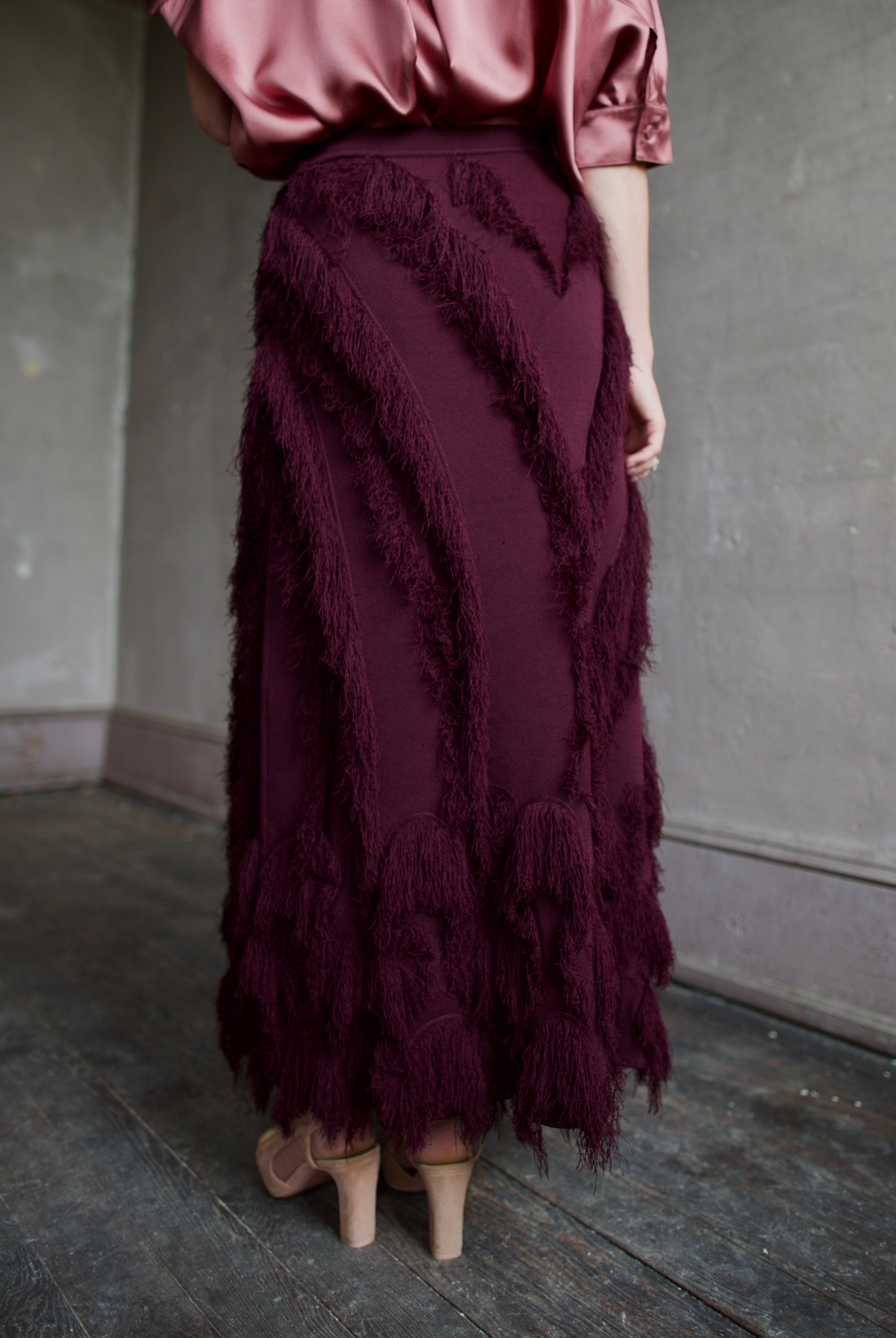 Mature model wearing a long burgundy skirt with a playful textured fringe pattern that can easily be dressed up or down