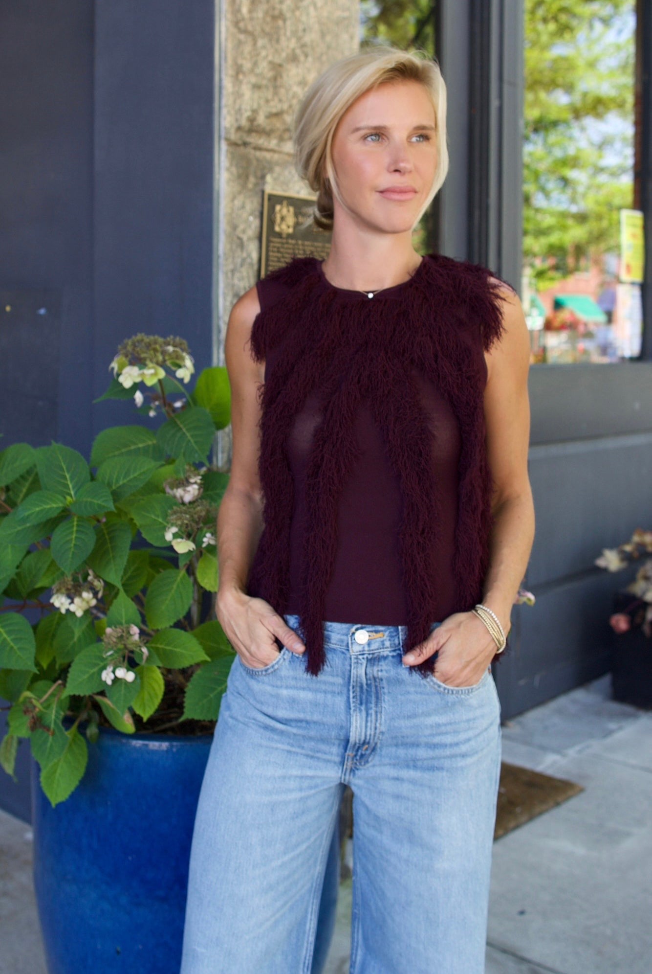 Model wearing The Bonnie Sleeveless Top by Ulla Johnson features a sleeveless fit and fringe detailing in a mahogany color.