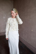 Mature model wearing designer jacket by Ulla Johnson. This delicate white lace button down jacket features an embroidered floral design