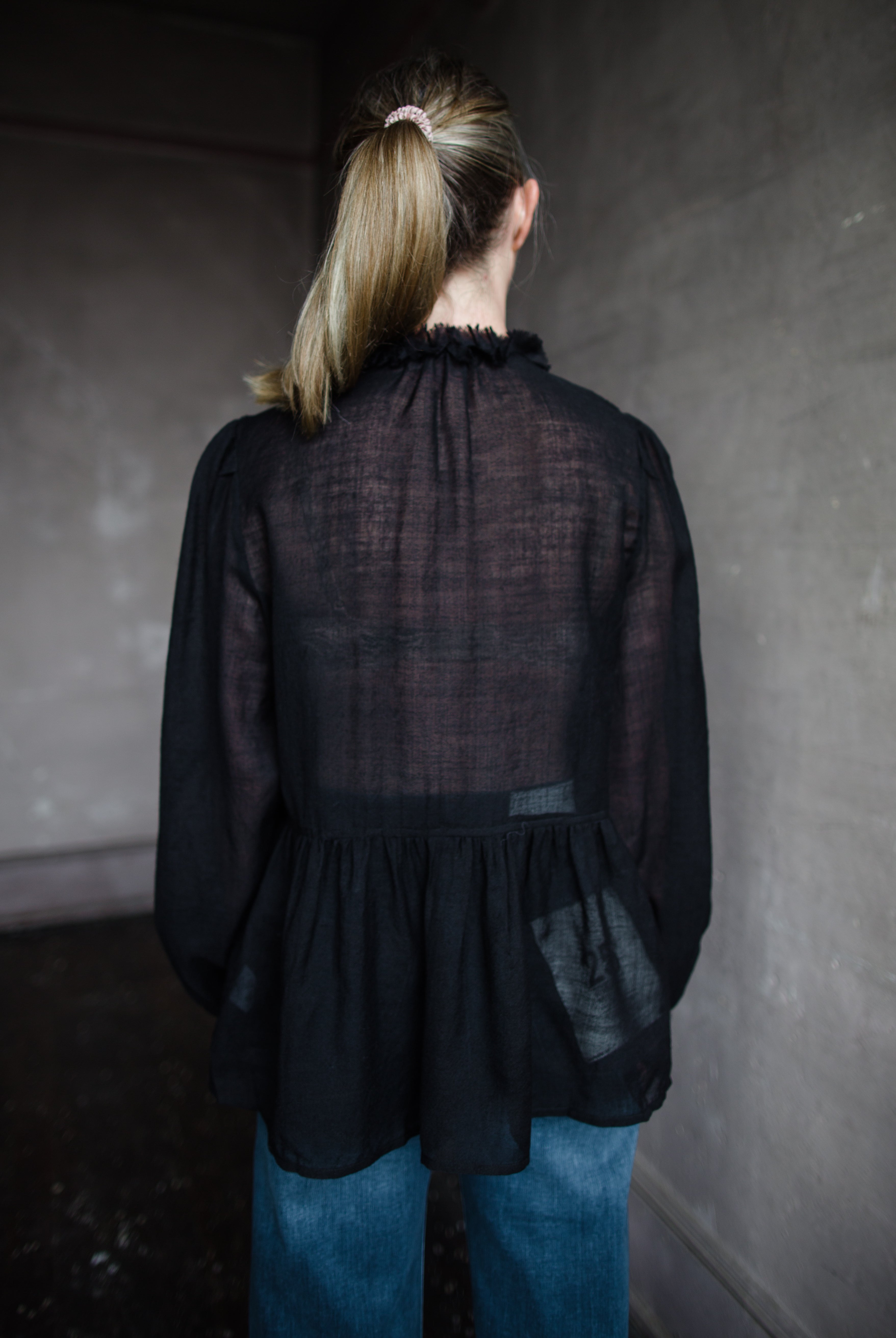 Image features woman wearing The Cosima Tunic by Ulla Johnson in Noir features a button down v neckline with rows of ruffles and iridescent sea shell buttons.