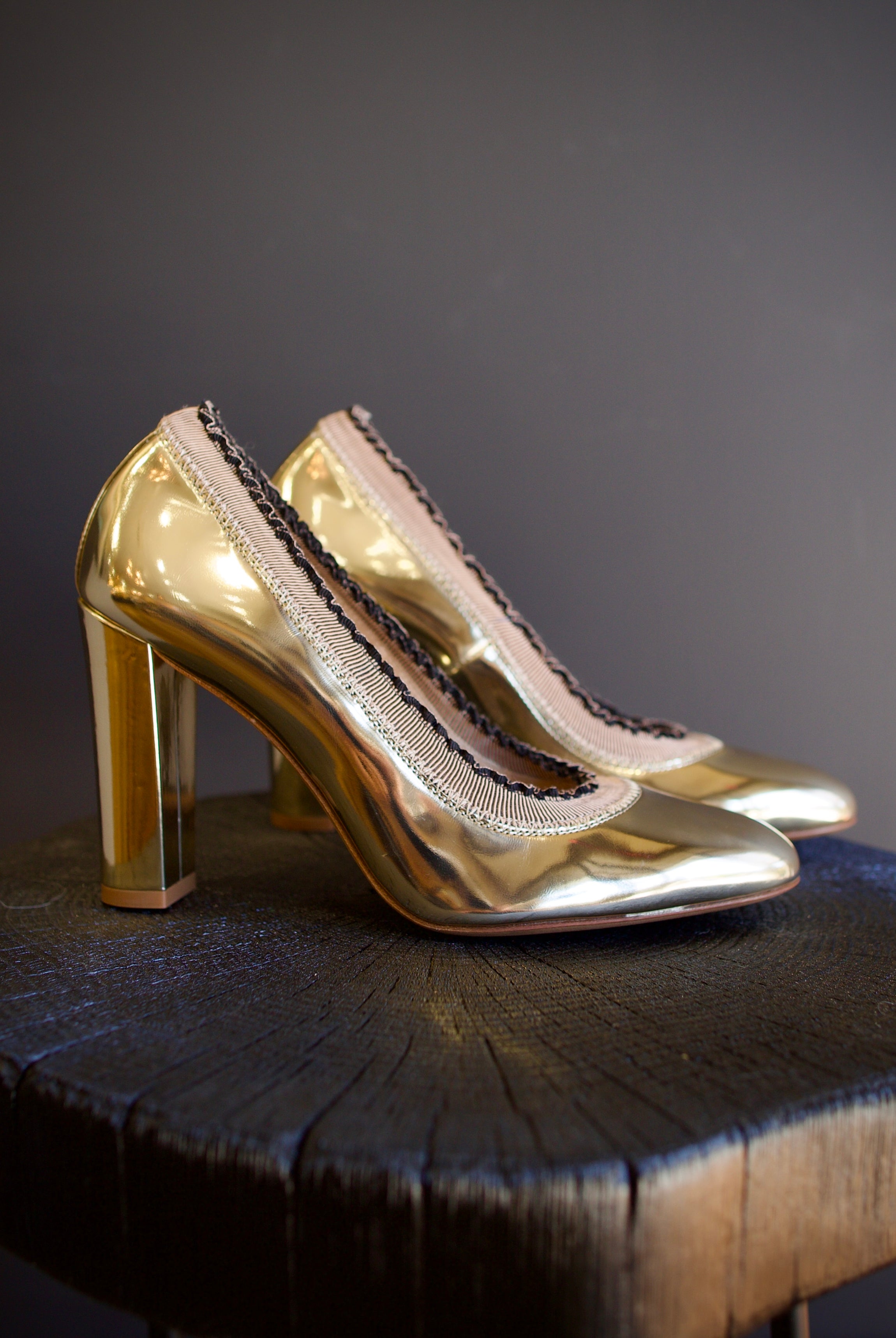 Image of the Elise Ruffle Pumps by Ulla Johnson feature a round toe and black tipped ruffle detailing in a polished gold color finish called platinum.
