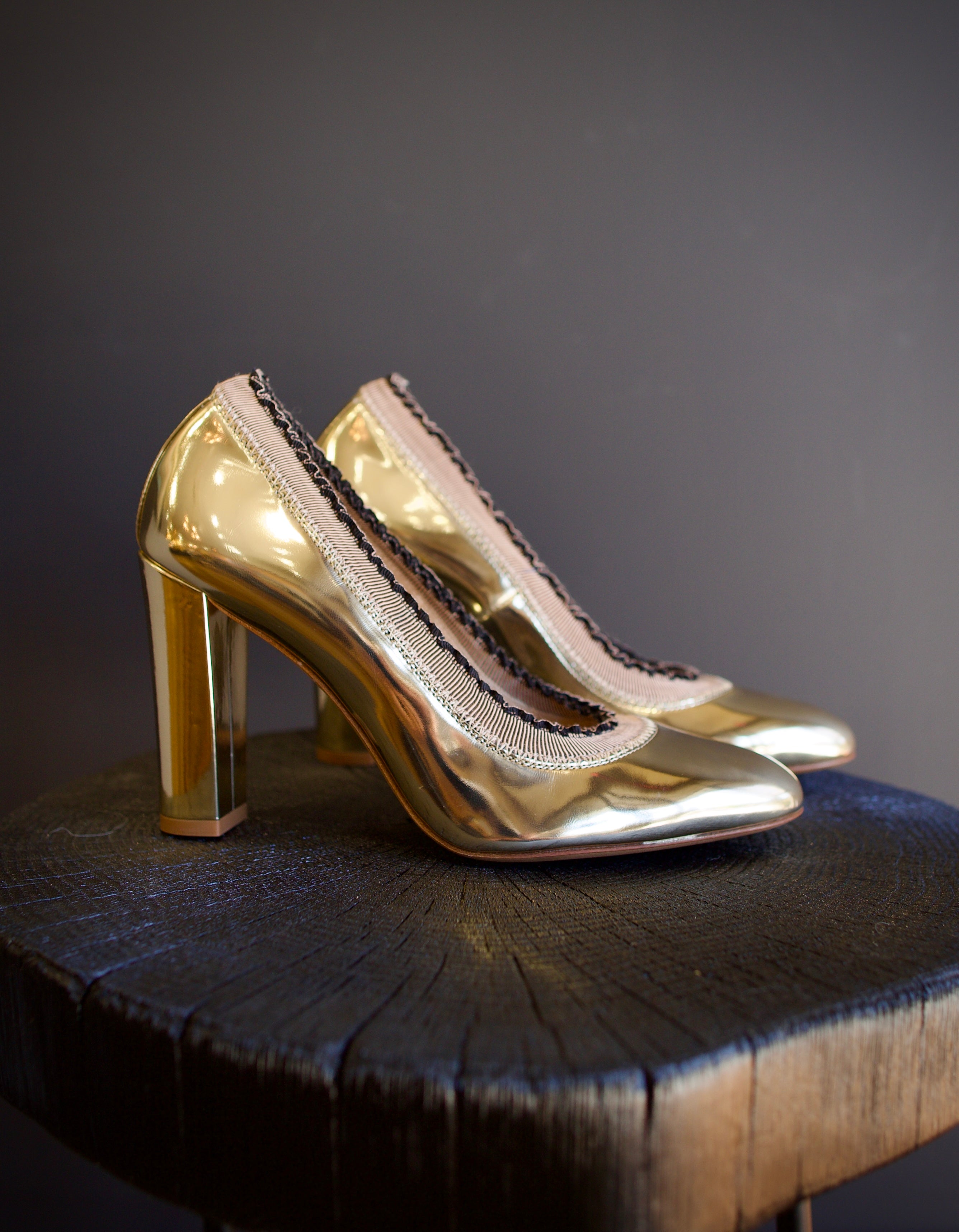 Image of the Elise Ruffle Pumps by Ulla Johnson feature a round toe and black tipped ruffle detailing in a polished gold color finish called platinum.