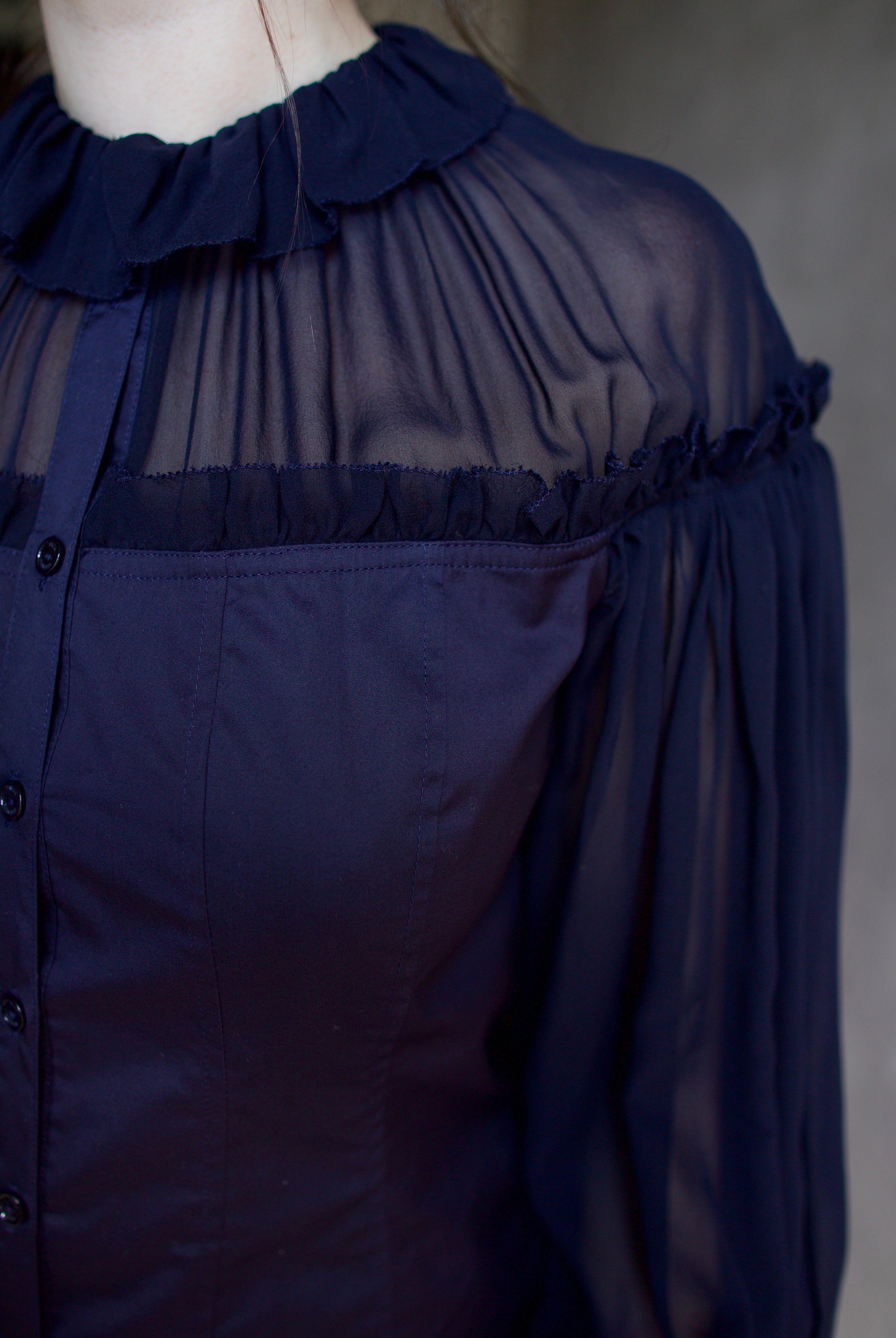 Detail photo of woman wearing a dark blue cotton and silk blouse with sheer long sleeves by designer Ulla Johnson