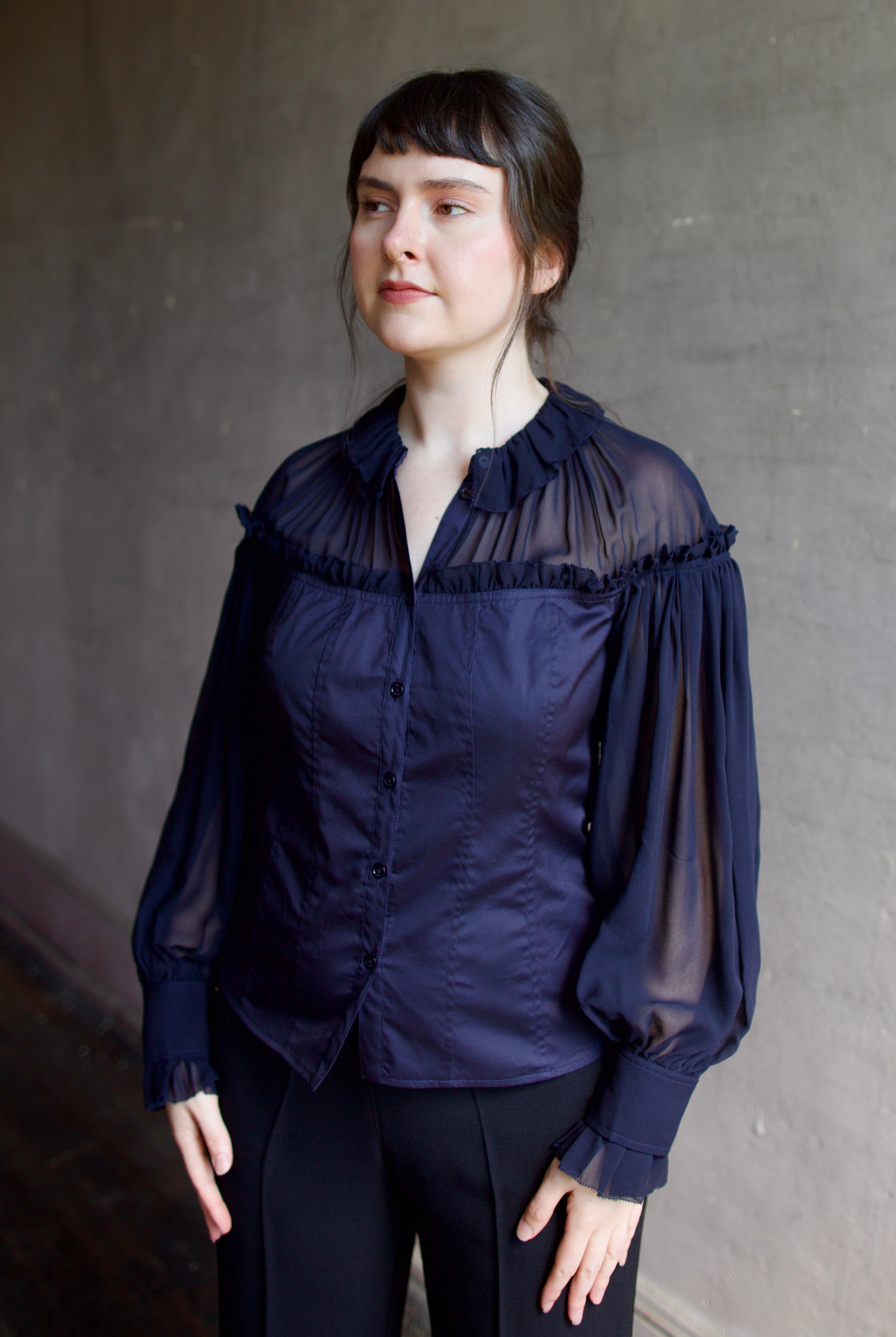 Woman wearing a dark blue cotton and silk blouse with sheer long sleeves by designer Ulla Johnson