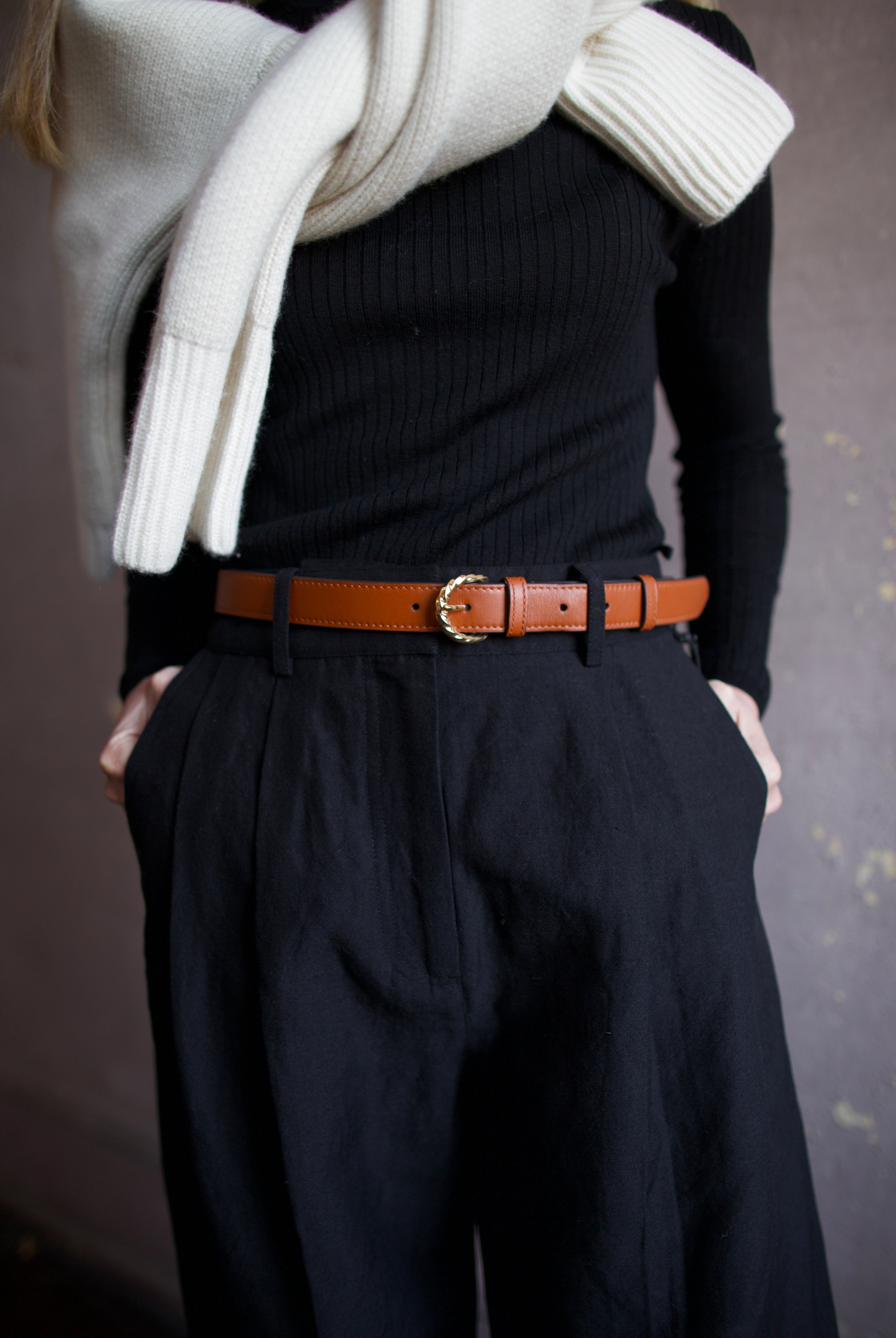 close up image of a woman wearing the Ulla Johnson gia belt, Apiece Apart merino sweater and mirabelle trousers and Naadam ultraluxe sweater