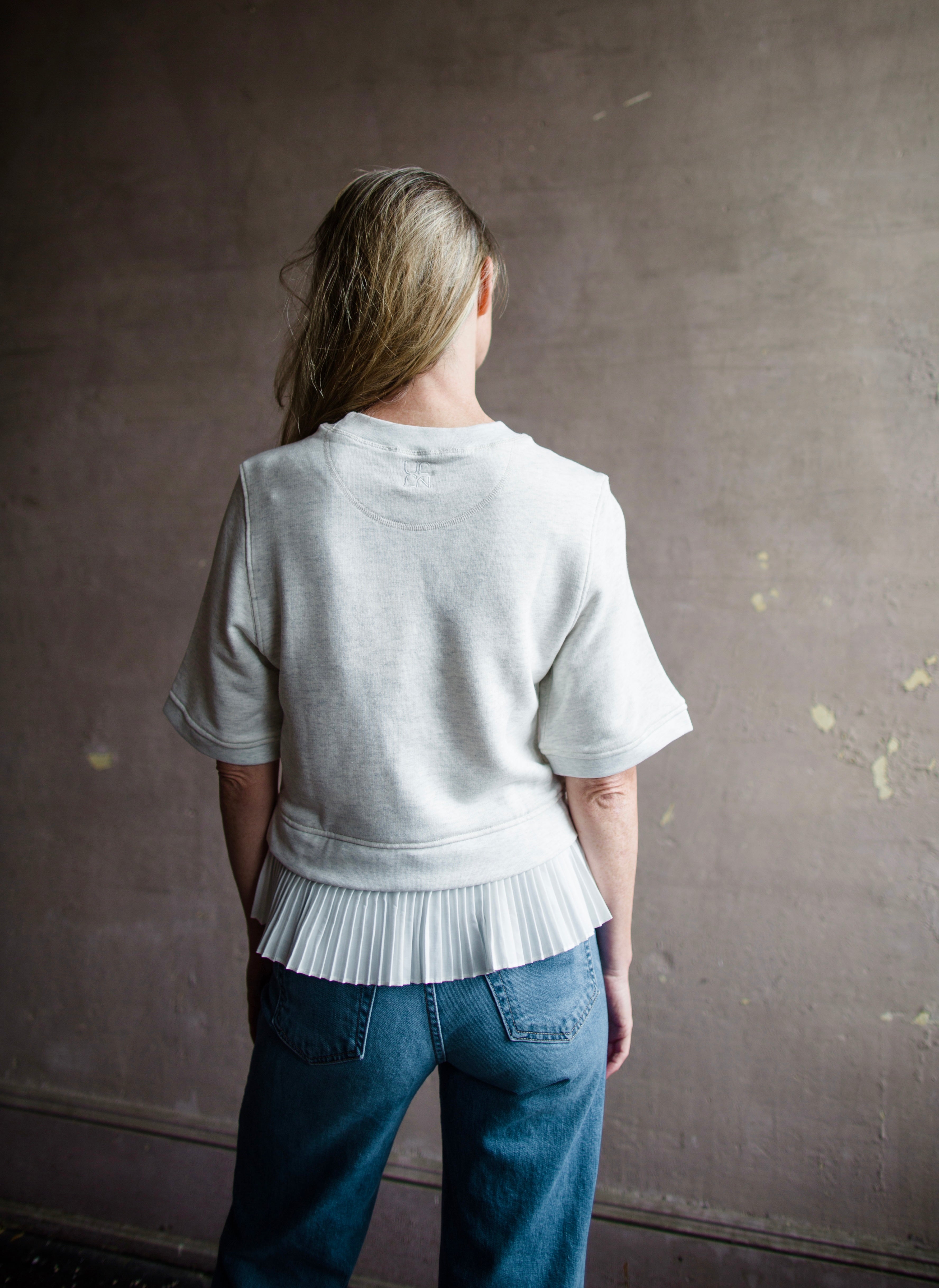Mature woman wearing the Ulla Johnson Harper Top grey short sleeve sweatshirt with layered white top