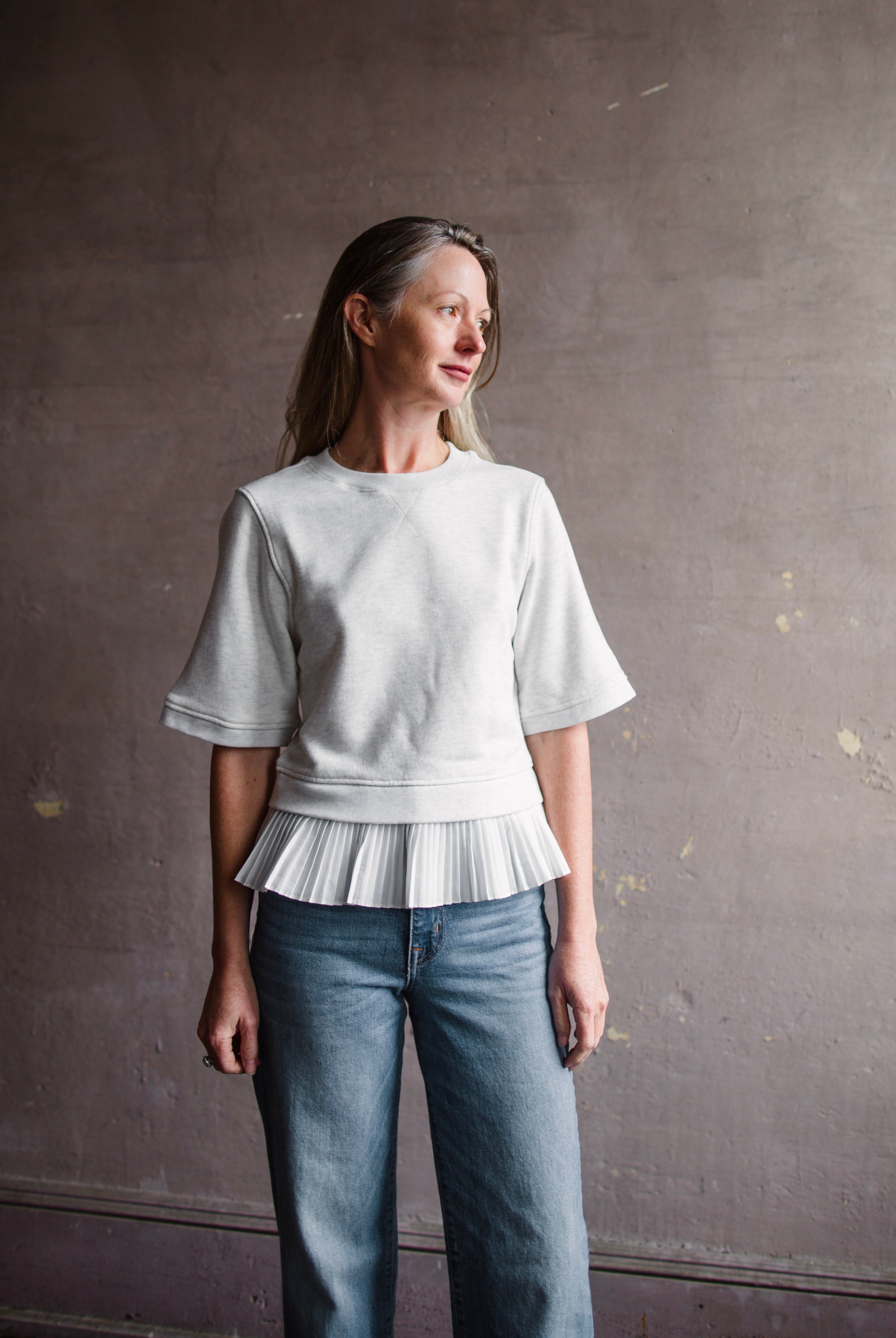 Mature woman wearing the Ulla Johnson Harper Top grey short sleeve sweatshirt with layered white top
