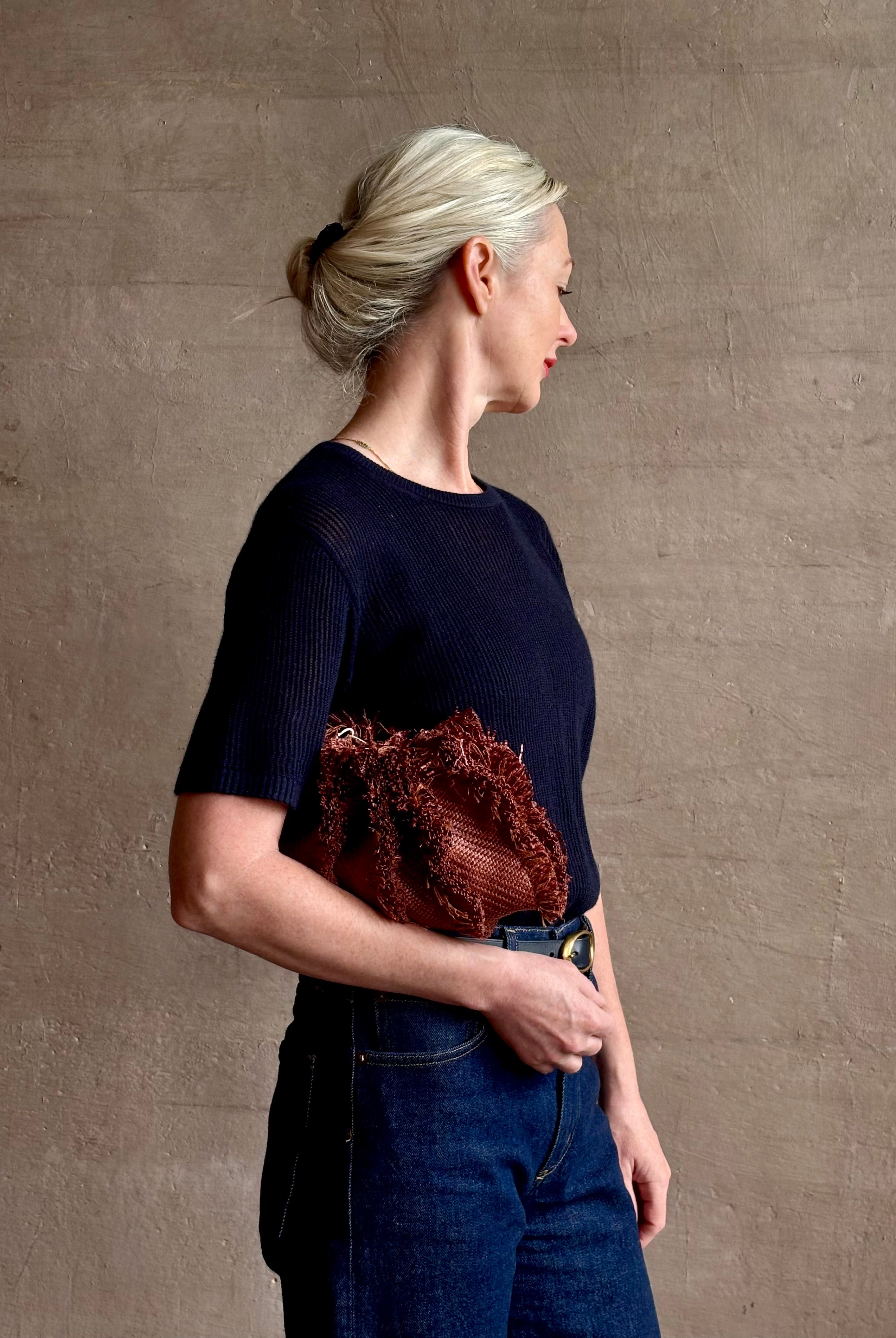 Mature woman with designer Ulla Johnson Adria crossbody bag with raffia-textured exterior and removeable handle that can double as a clutch in a warm brown neutral tone