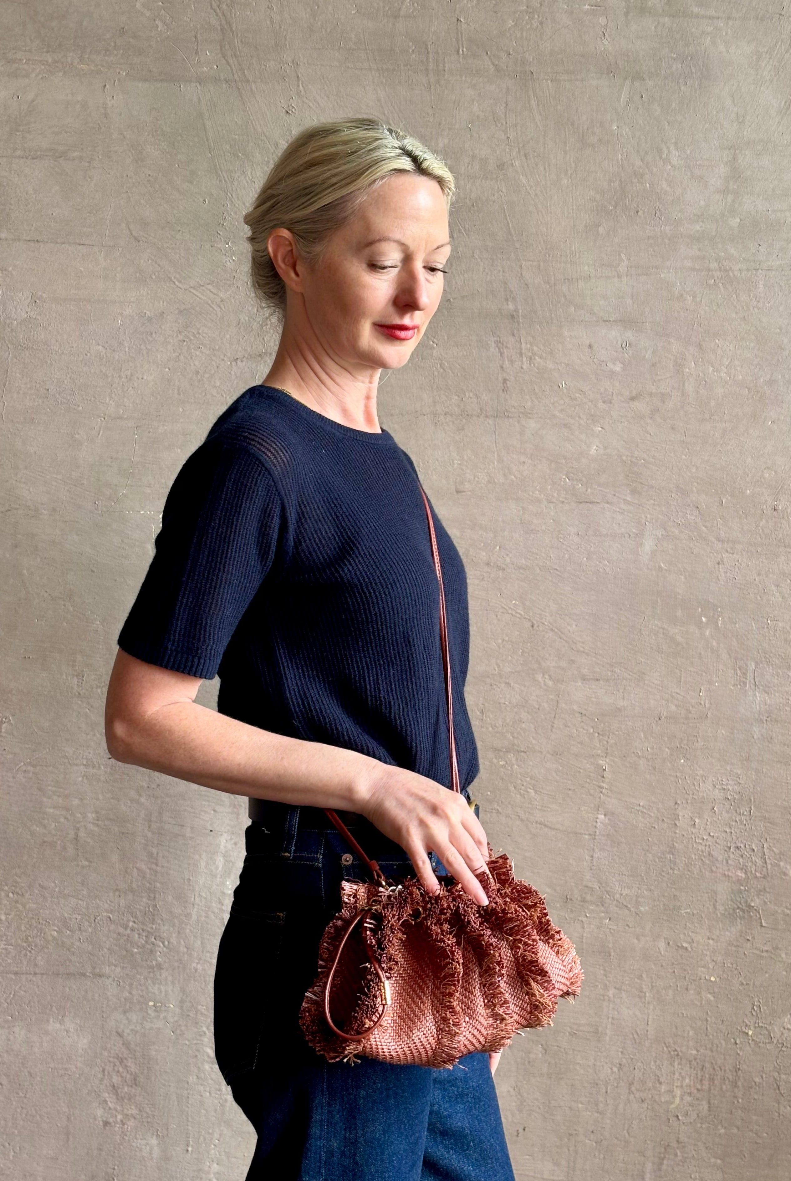 Mature woman with designer Ulla Johnson Adria crossbody bag with raffia-textured exterior and removeable handle that can double as a clutch in a warm brown neutral tone