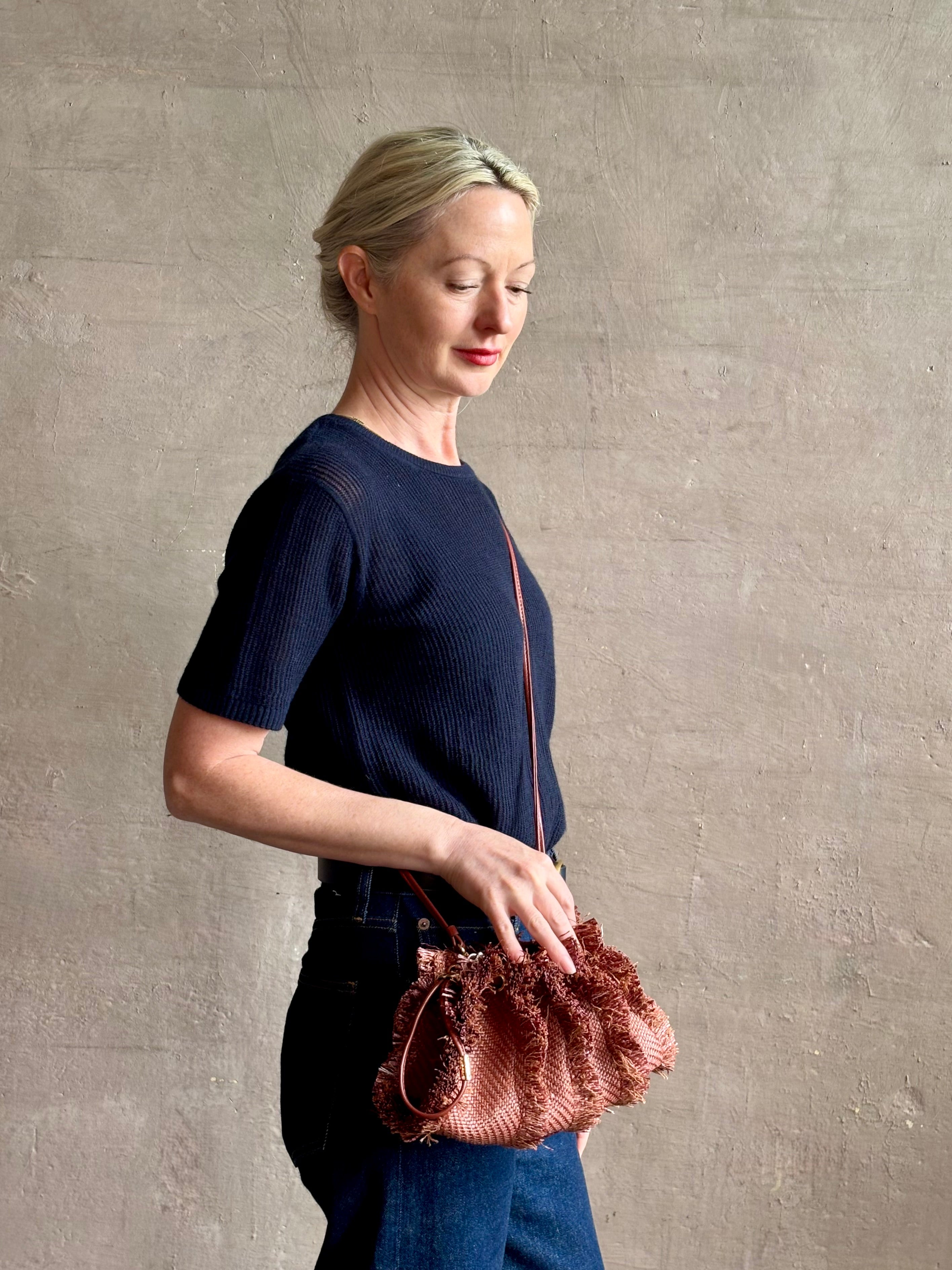 Mature woman with designer Ulla Johnson Adria crossbody bag with raffia-textured exterior and removeable handle that can double as a clutch in a warm brown neutral tone