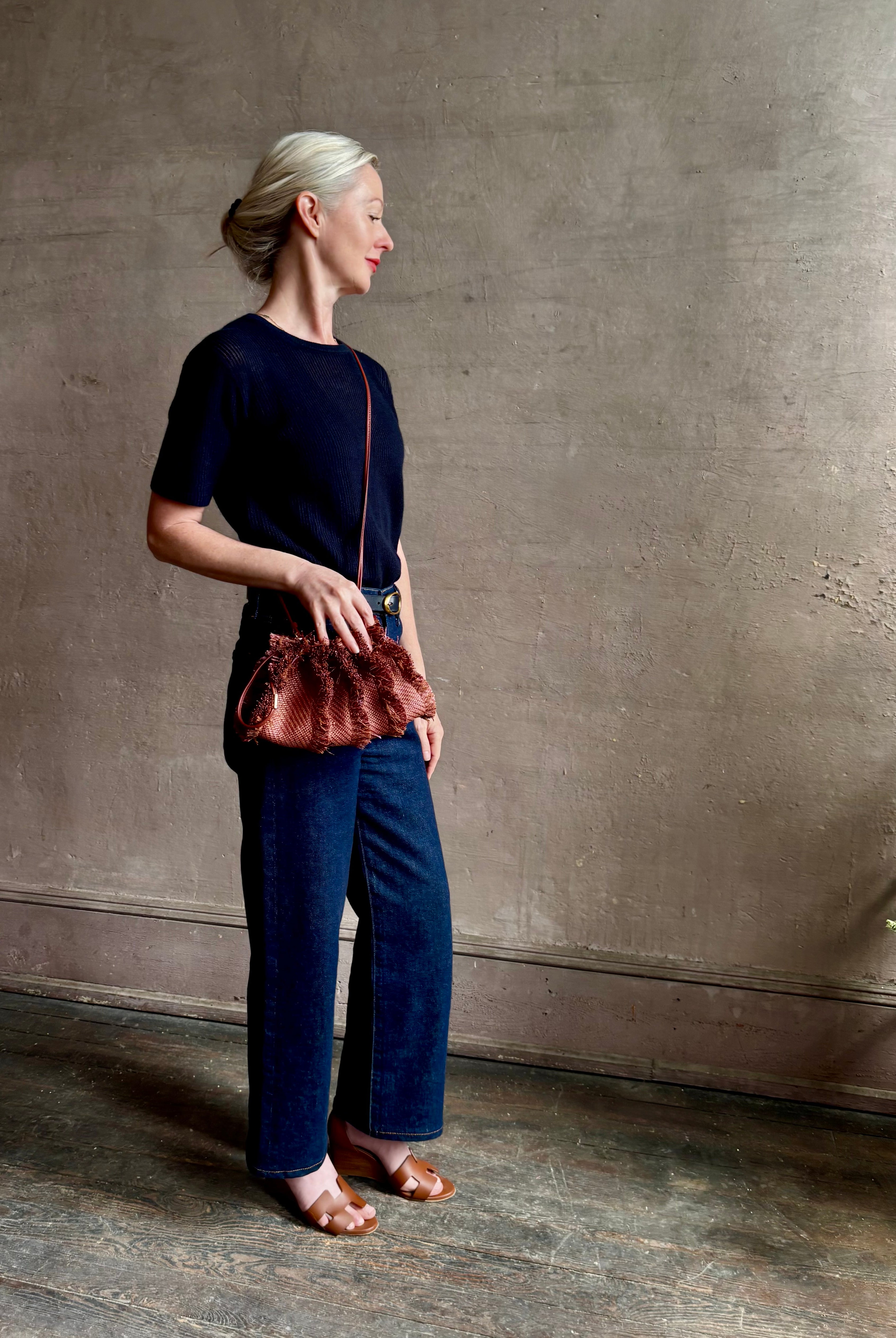 Mature woman with designer Ulla Johnson Adria crossbody bag with raffia-textured exterior and removeable handle that can double as a clutch in a warm brown neutral tone