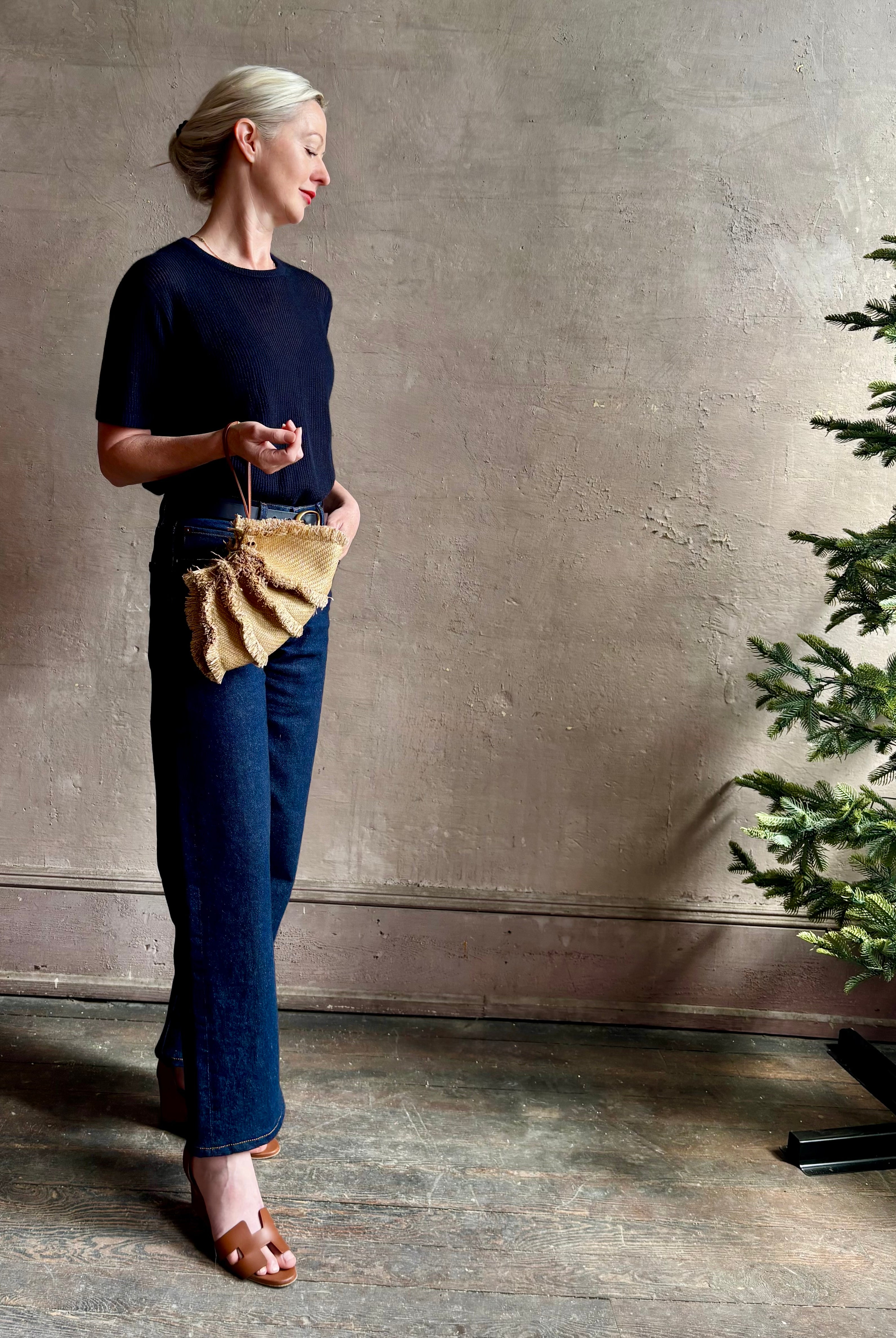 Mature woman with designer Ulla Johnson Adria crossbody bag with raffia-textured exterior and removeable handle that can double as a clutch in a natural raffia tone