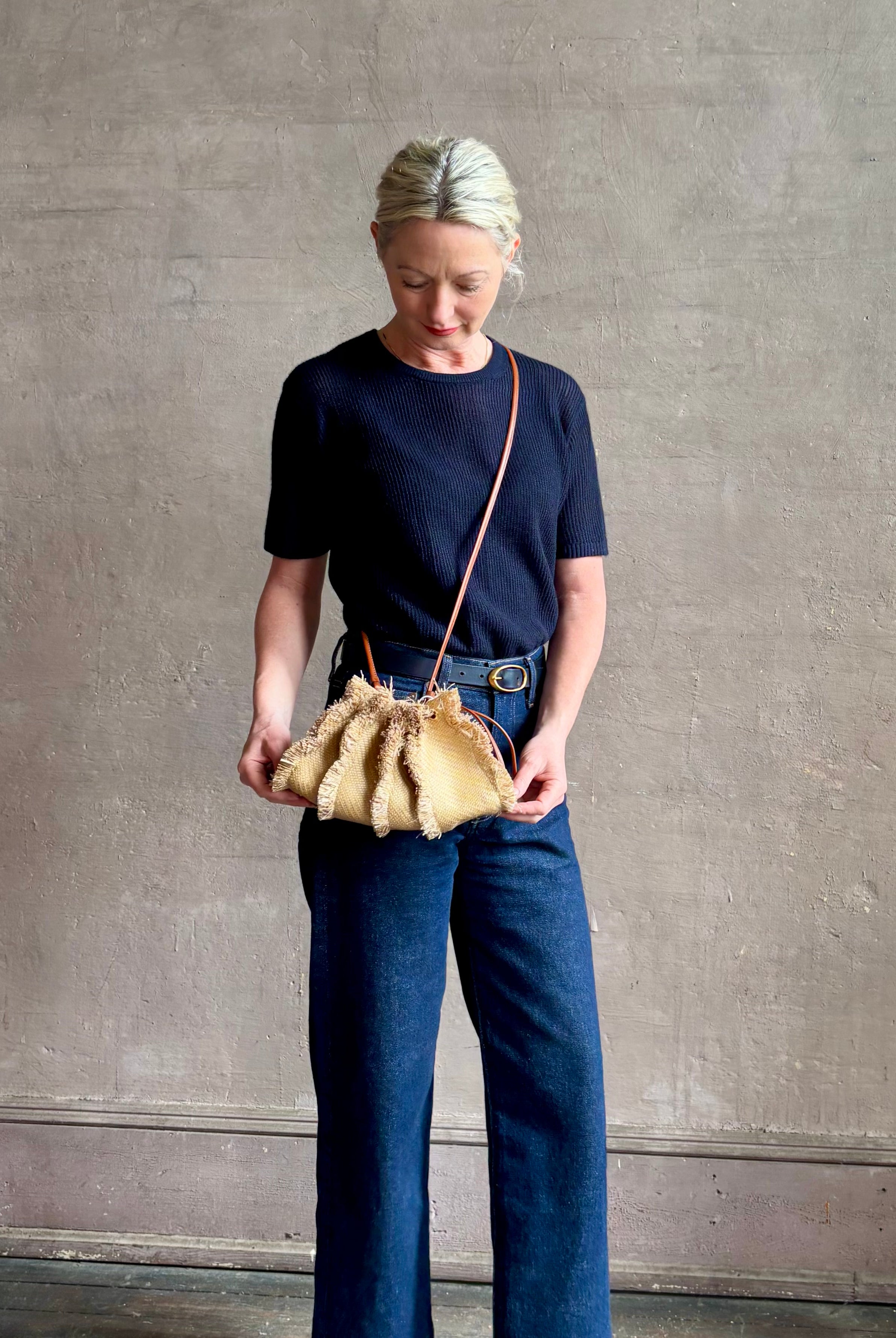 Mature woman with designer Ulla Johnson Adria crossbody bag with raffia-textured exterior and removeable handle that can double as a clutch in a natural raffia tone