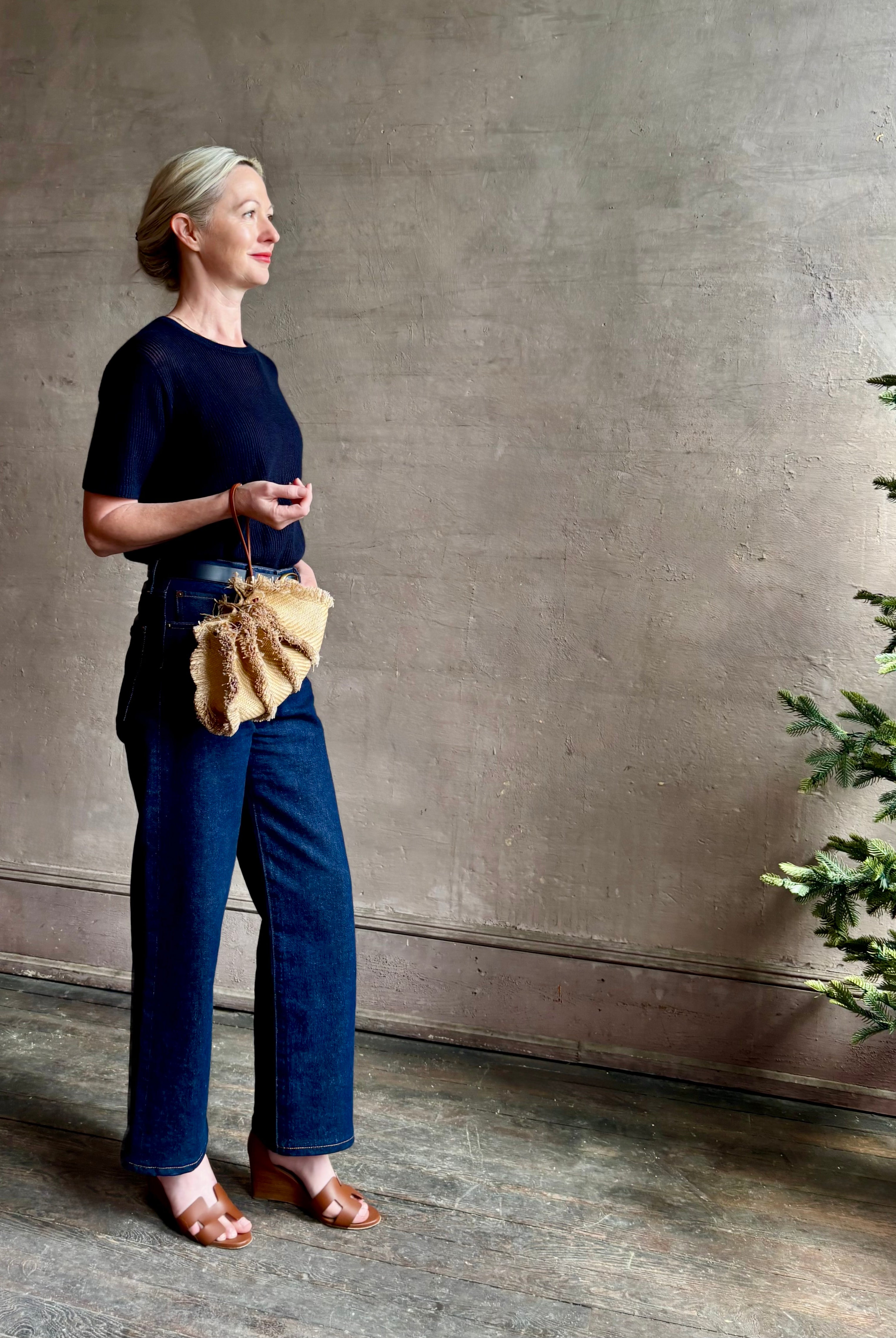 Mature woman with designer Ulla Johnson Adria crossbody bag with raffia-textured exterior and removeable handle that can double as a clutch in a natural raffia tone