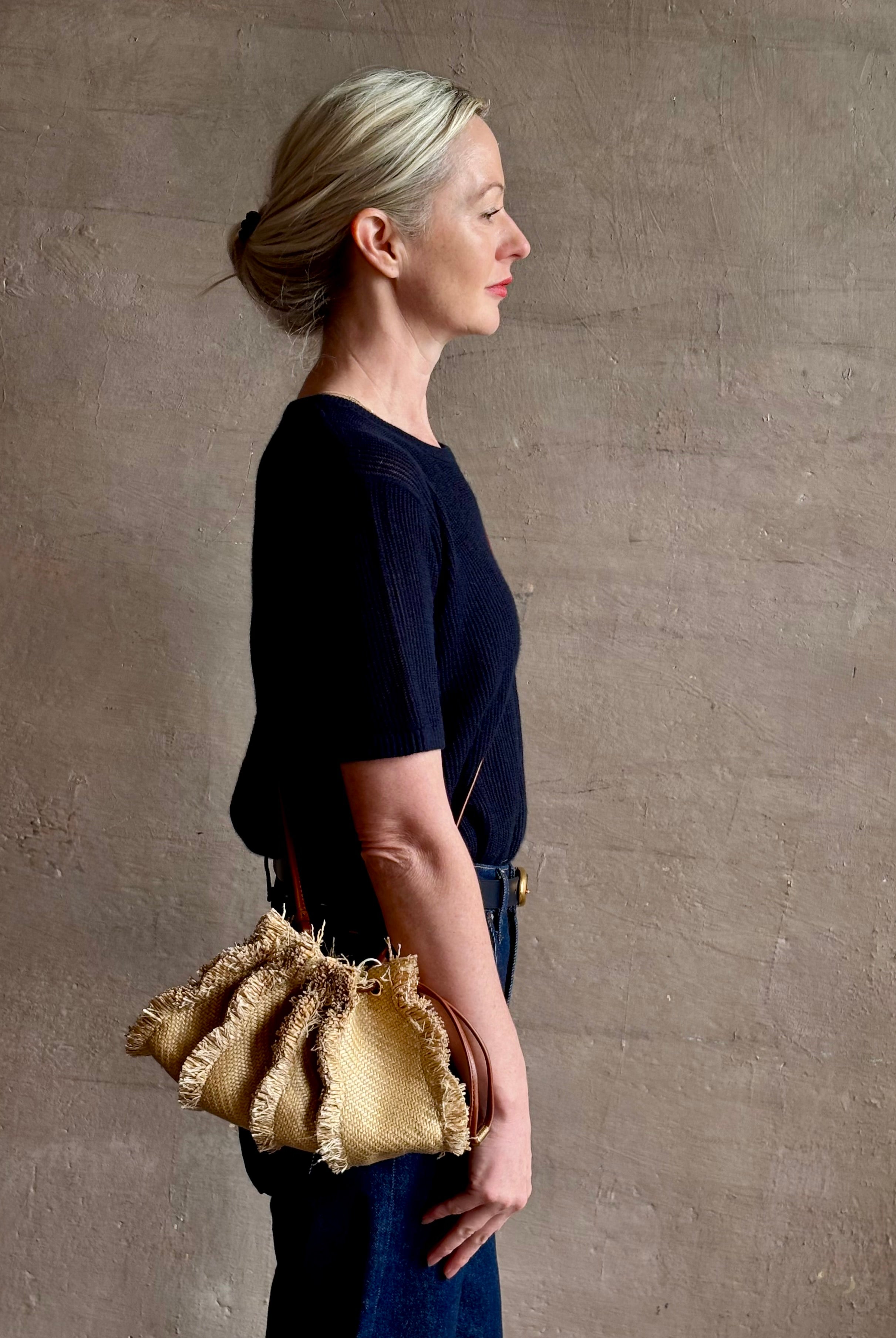 Mature woman with designer Ulla Johnson Adria crossbody bag with raffia-textured exterior and removeable handle that can double as a clutch in a natural raffia tone