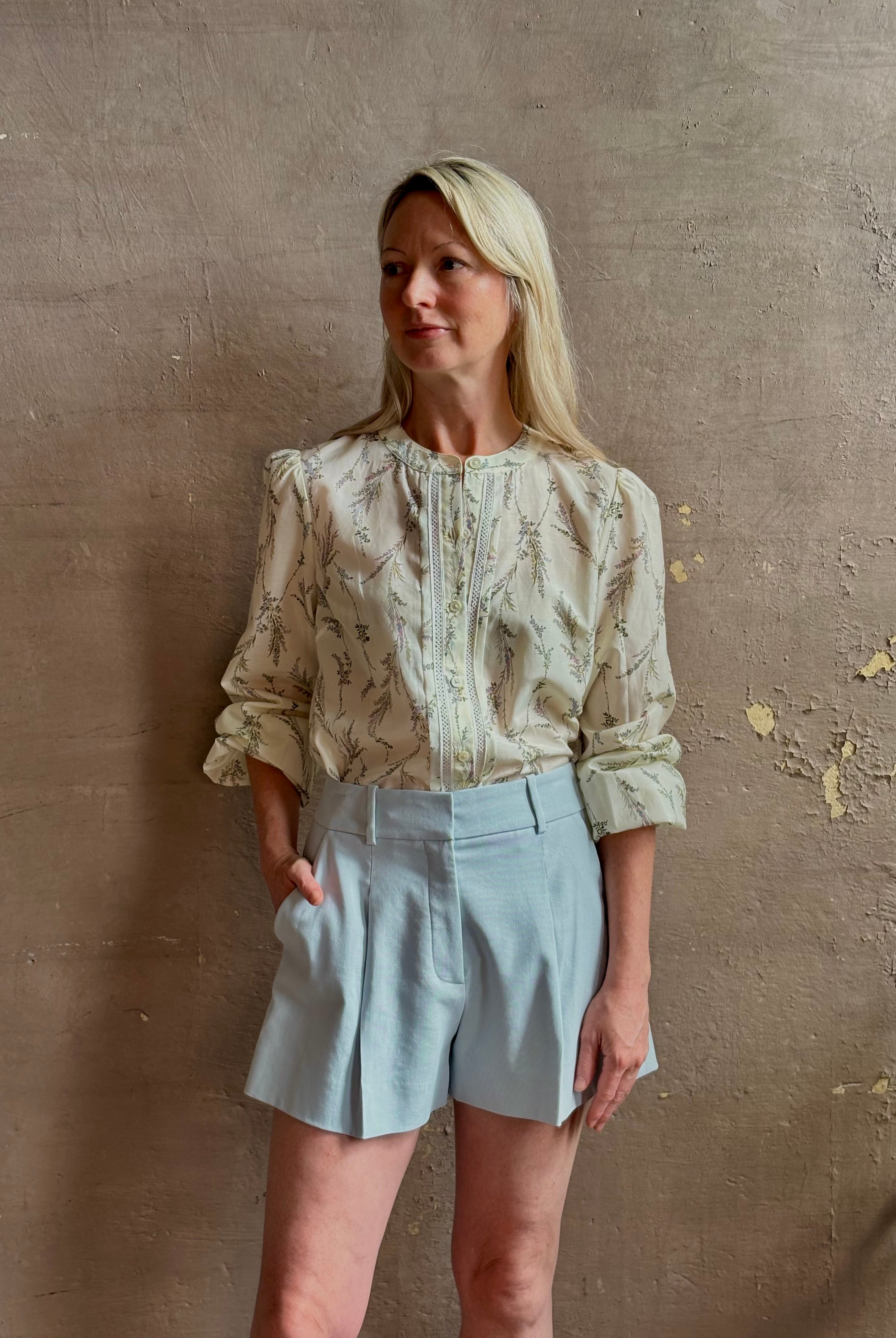 Mature woman wearing elevated Craig Short from Veronica Beard a sophisticated women's designer short rendered in river mist light blue and crafted from a refined blend of cotton and viscose with side pockets, one front pleat and tailored waistband with belt loops