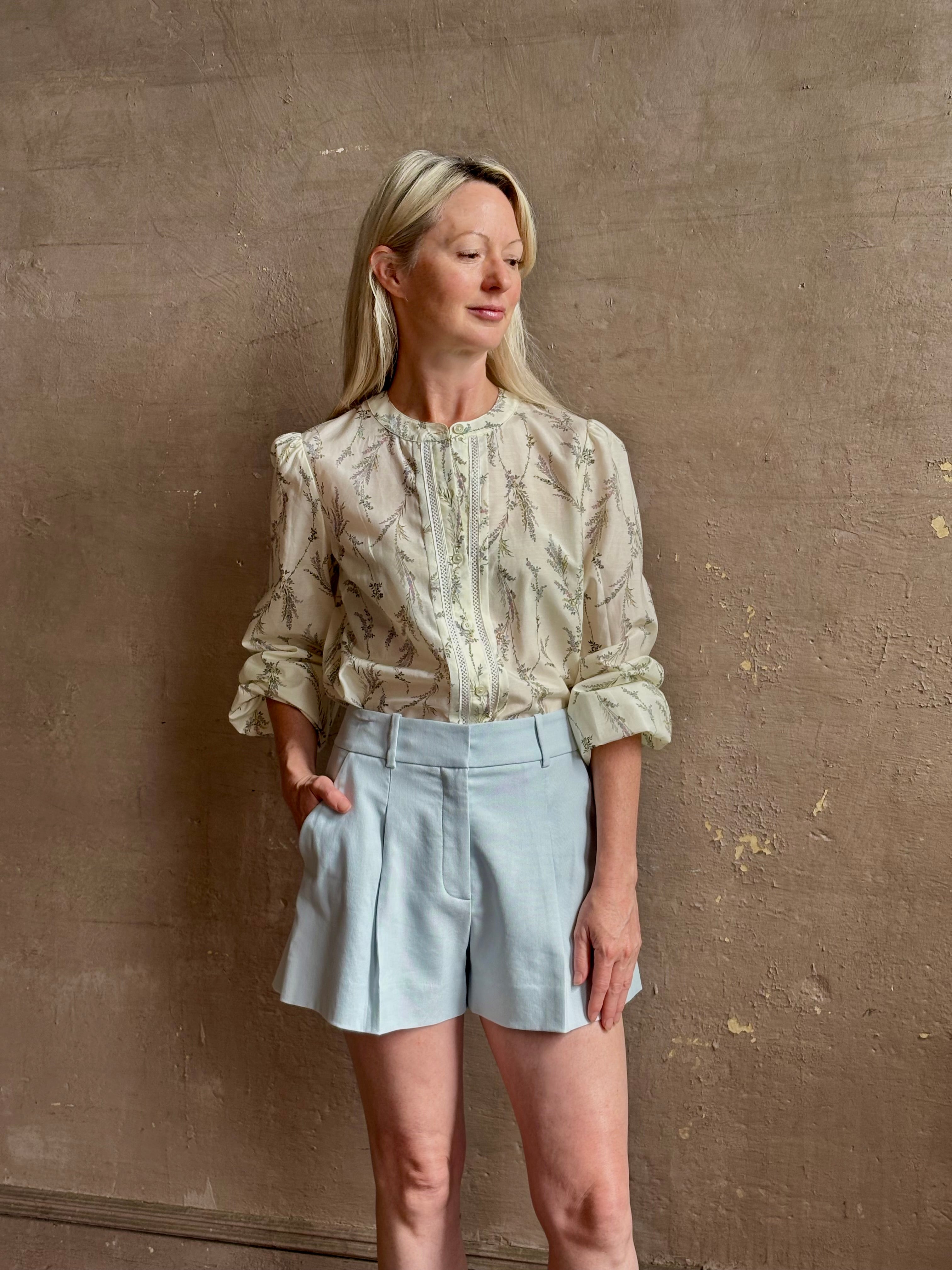 Mature woman wearing elevated Craig Short from Veronica Beard a sophisticated women's designer short rendered in river mist light blue and crafted from a refined blend of cotton and viscose with side pockets, one front pleat and tailored waistband with belt loops