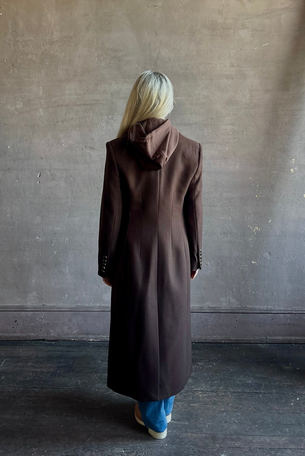 Mature woman wearing Veronica Beard Elspeth Coat with OVS Hoodie Dickey in Espresso brown wool-cashmere A-line coat with a removable hoodie layer. Playful, sculptural cold-weather luxury.
