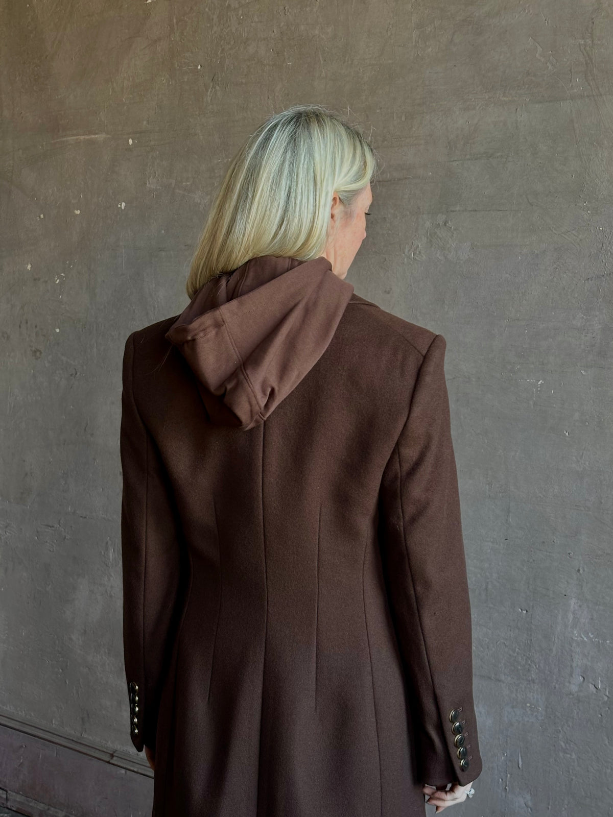 Mature woman wearing Veronica Beard Elspeth Coat with OVS Hoodie Dickey in Espresso brown wool-cashmere A-line coat with a removable hoodie layer. Playful, sculptural cold-weather luxury.