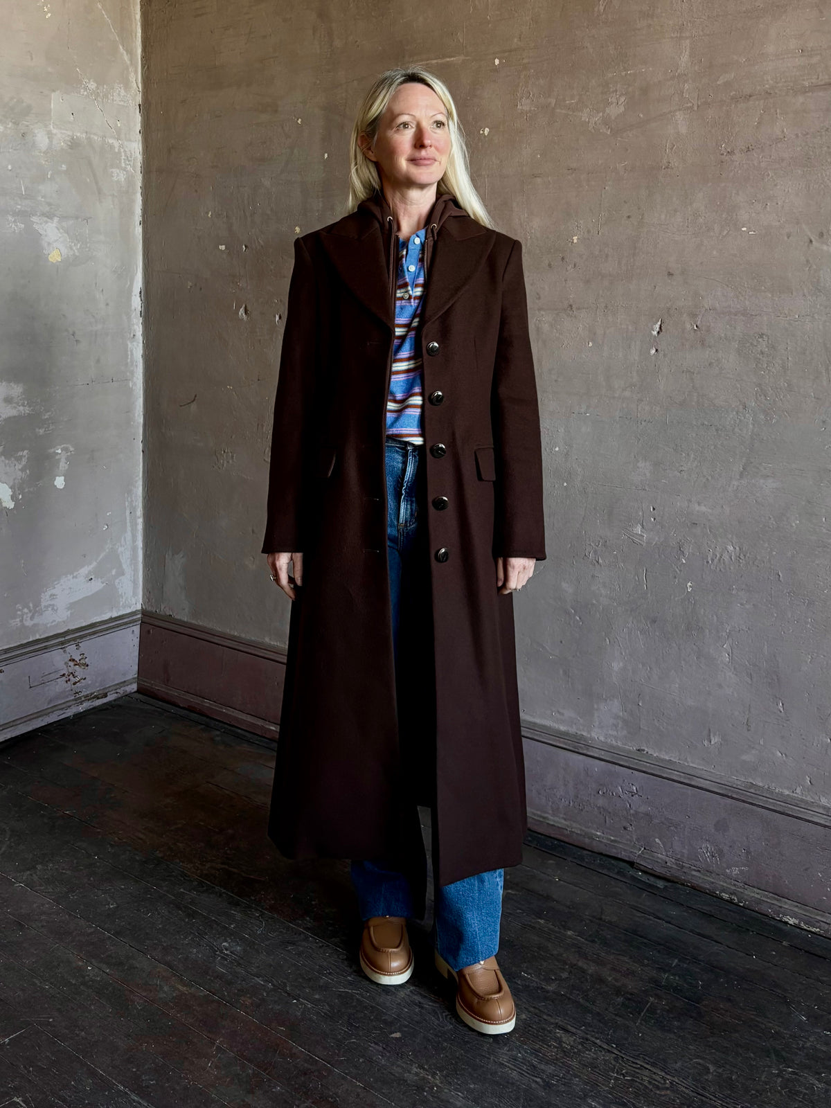 Mature woman wearing Veronica Beard Elspeth Coat with OVS Hoodie Dickey in Espresso brown wool-cashmere A-line coat with a removable hoodie layer. Playful, sculptural cold-weather luxury.