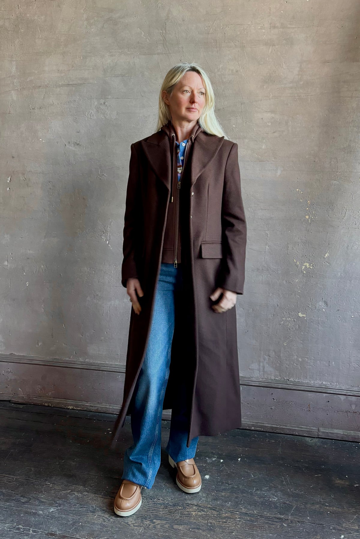 Mature woman wearing Veronica Beard Elspeth Coat with OVS Hoodie Dickey in Espresso brown wool-cashmere A-line coat with a removable hoodie layer. Playful, sculptural cold-weather luxury.