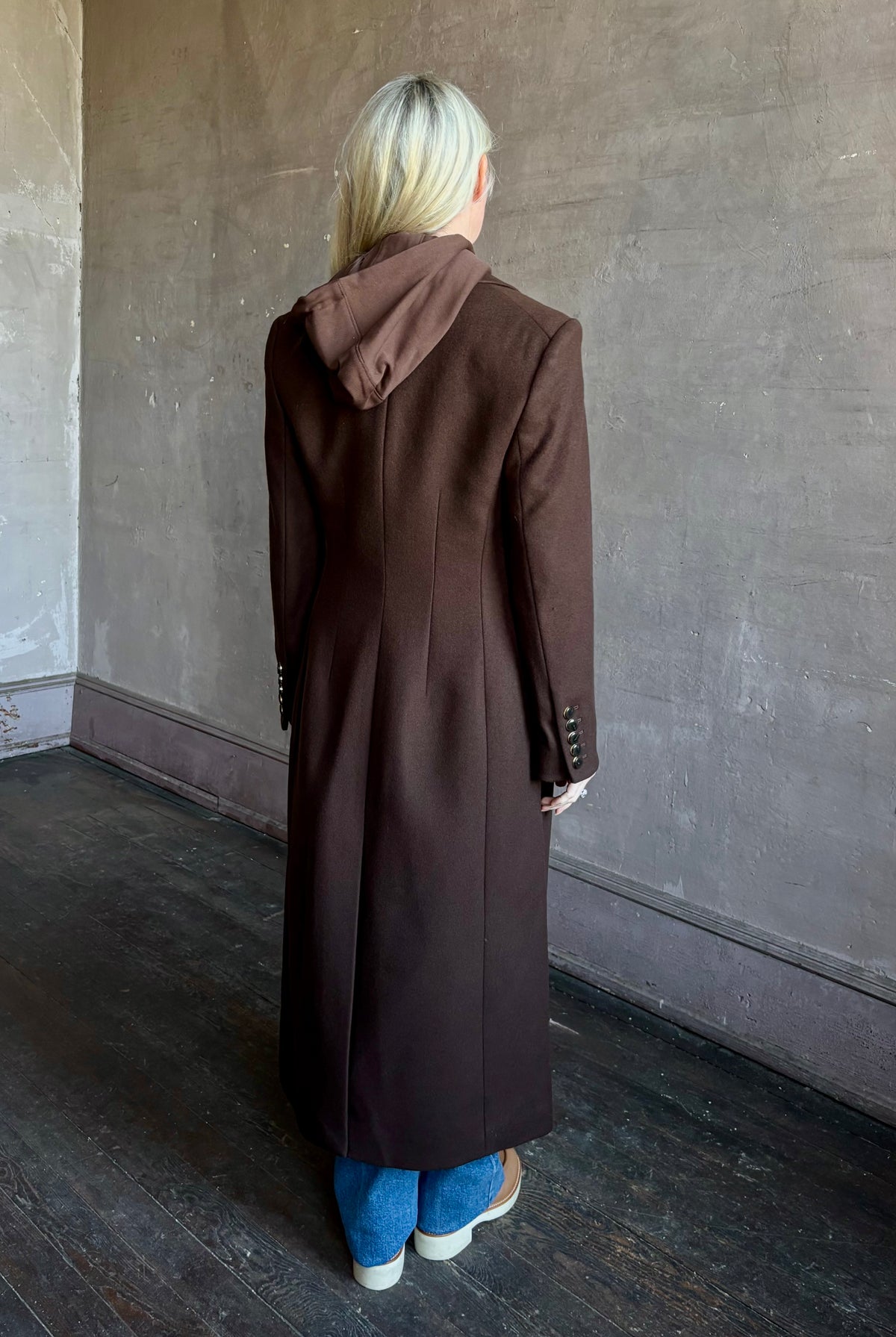 Mature woman wearing Veronica Beard Elspeth Coat with OVS Hoodie Dickey in Espresso brown wool-cashmere A-line coat with a removable hoodie layer. Playful, sculptural cold-weather luxury.