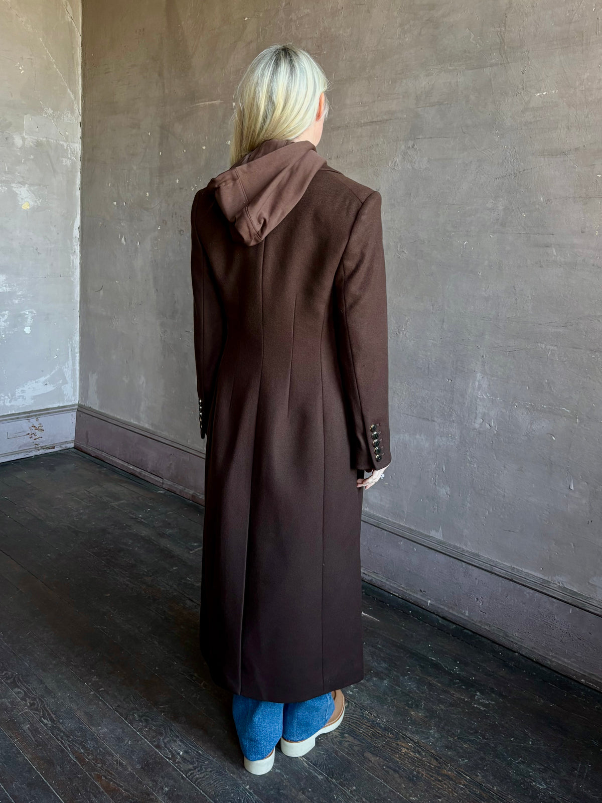 Mature woman wearing Veronica Beard Elspeth Coat with OVS Hoodie Dickey in Espresso brown wool-cashmere A-line coat with a removable hoodie layer. Playful, sculptural cold-weather luxury.