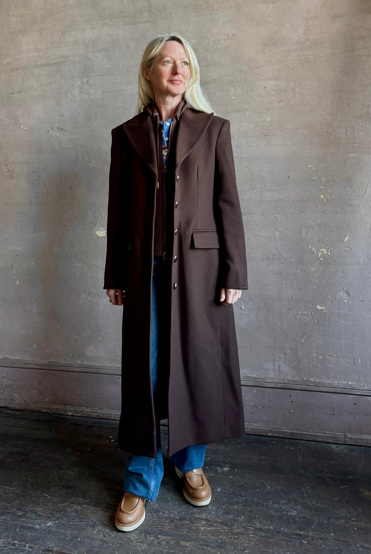 Mature woman wearing Veronica Beard Elspeth Coat with OVS Hoodie Dickey in Espresso brown wool-cashmere A-line coat with a removable hoodie layer. Playful, sculptural cold-weather luxury.