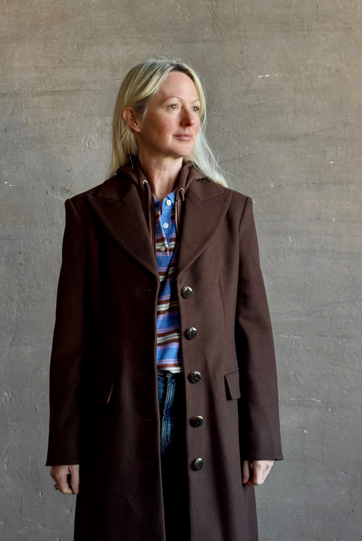 Mature woman wearing Veronica Beard Elspeth Coat with OVS Hoodie Dickey in Espresso brown wool-cashmere A-line coat with a removable hoodie layer. Playful, sculptural cold-weather luxury.