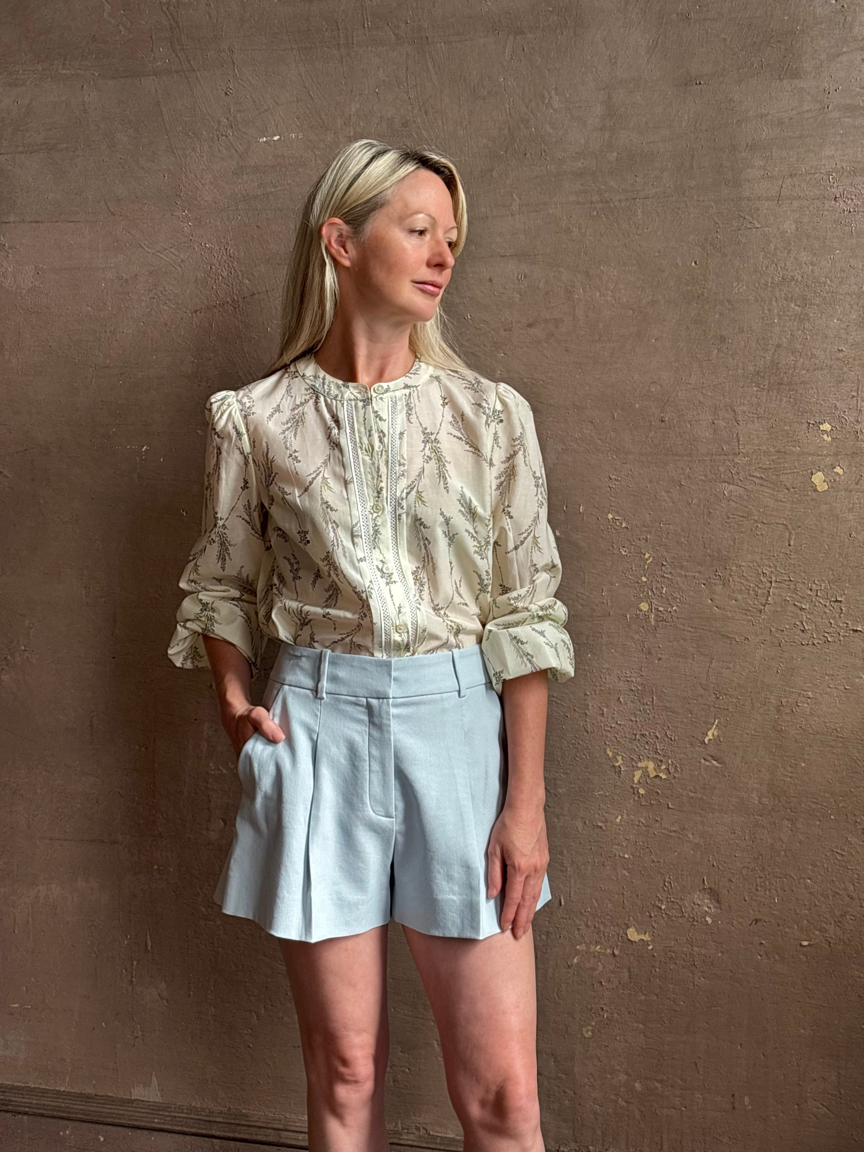Mature woman wearing luxurious tailored Emiko Blouse from Veronica Beard a women's designer blouse rendered in a cream ground adorned with a delicate prairie floral print and crafted from a cotton and silk blend with long sleeves, button front and round mandarin collar.