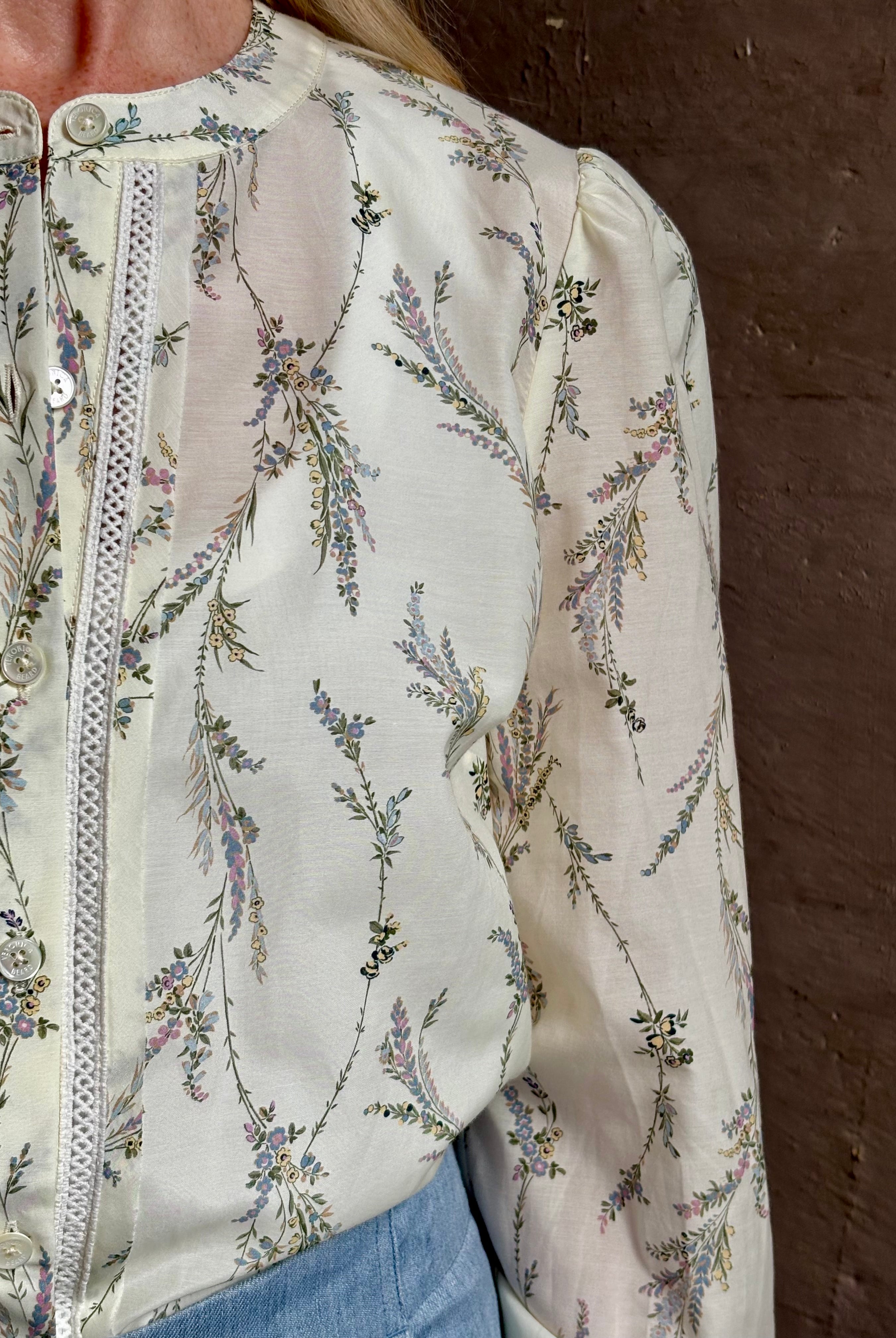 Mature woman wearing luxurious tailored Emiko Blouse from Veronica Beard a women's designer blouse rendered in a cream ground adorned with a delicate prairie floral print and crafted from a cotton and silk blend with long sleeves, button front and round mandarin collar.