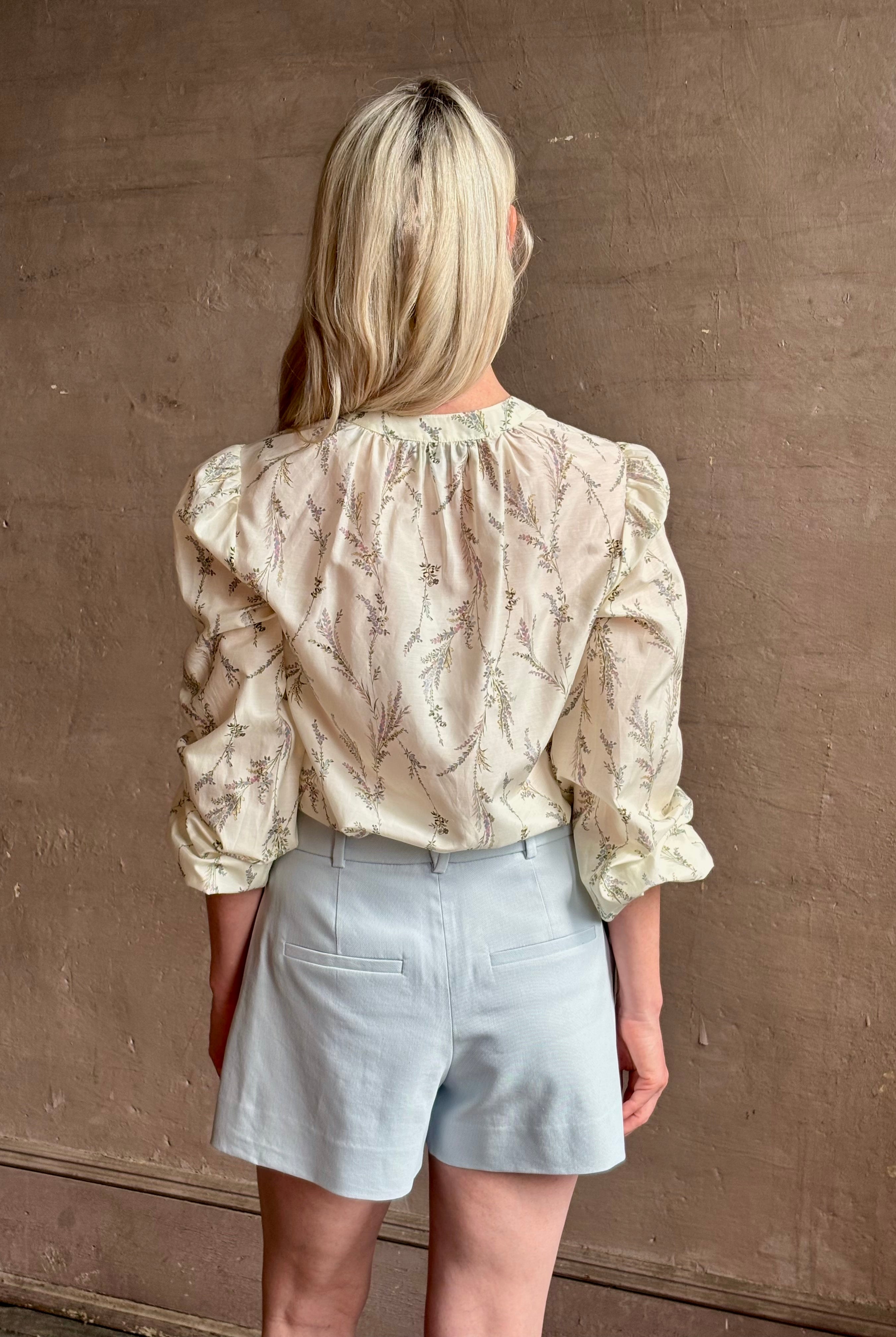 Mature woman wearing luxurious tailored Emiko Blouse from Veronica Beard a women's designer blouse rendered in a cream ground adorned with a delicate prairie floral print and crafted from a cotton and silk blend with long sleeves, button front and round mandarin collar.