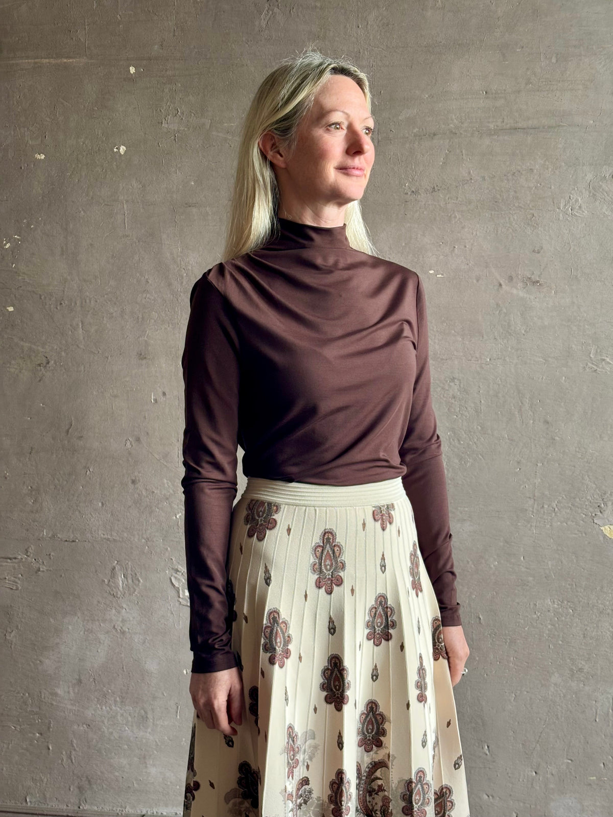 Mature woman wearing Veronica Beard's Mylie Top in Espresso brown lightweight lyocell with asymmetrical shoulder draping and side ruching