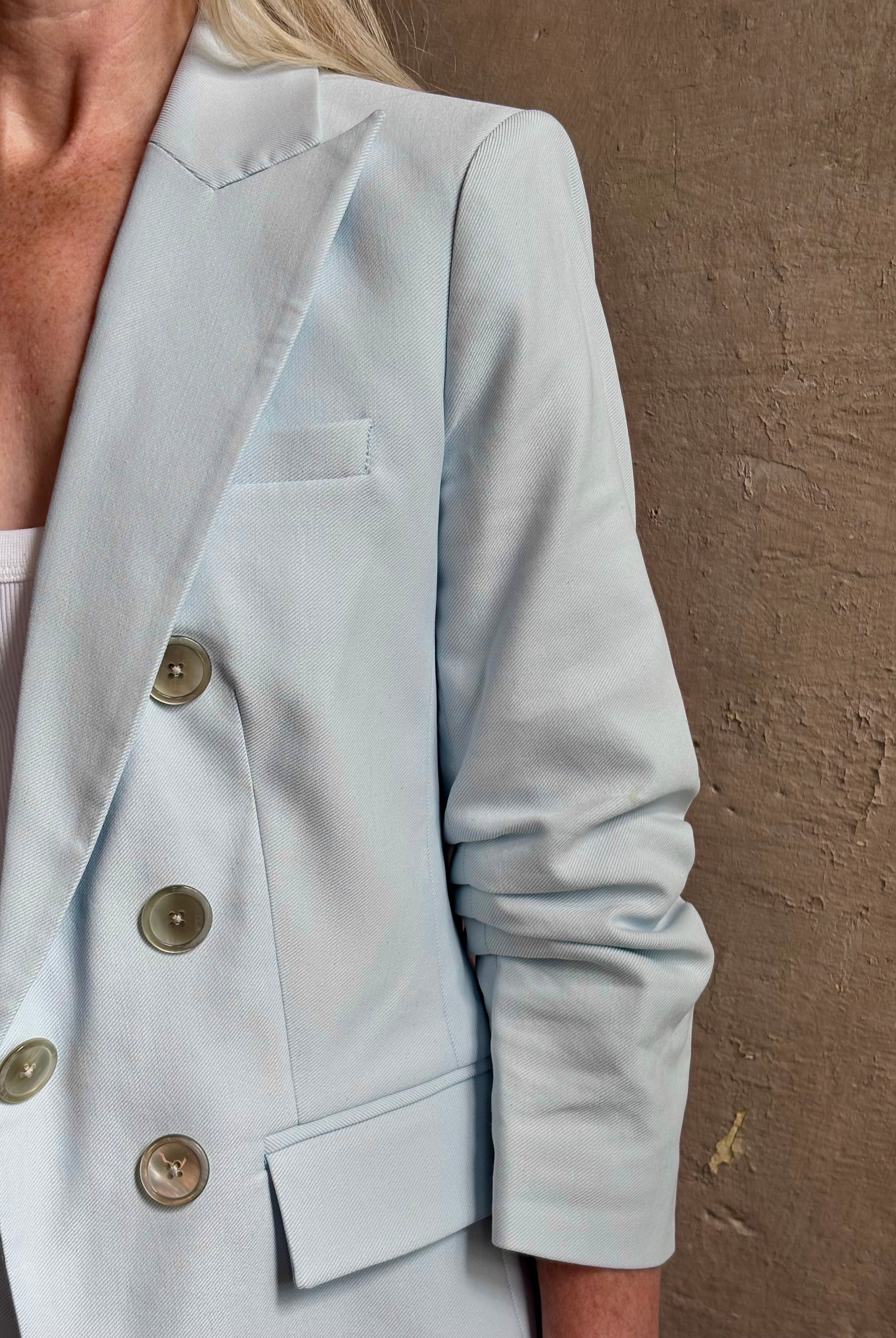 Mature woman wearing tailored Veronica Beard Tomi Dickey Jacket light blue ruched sleeves with button front