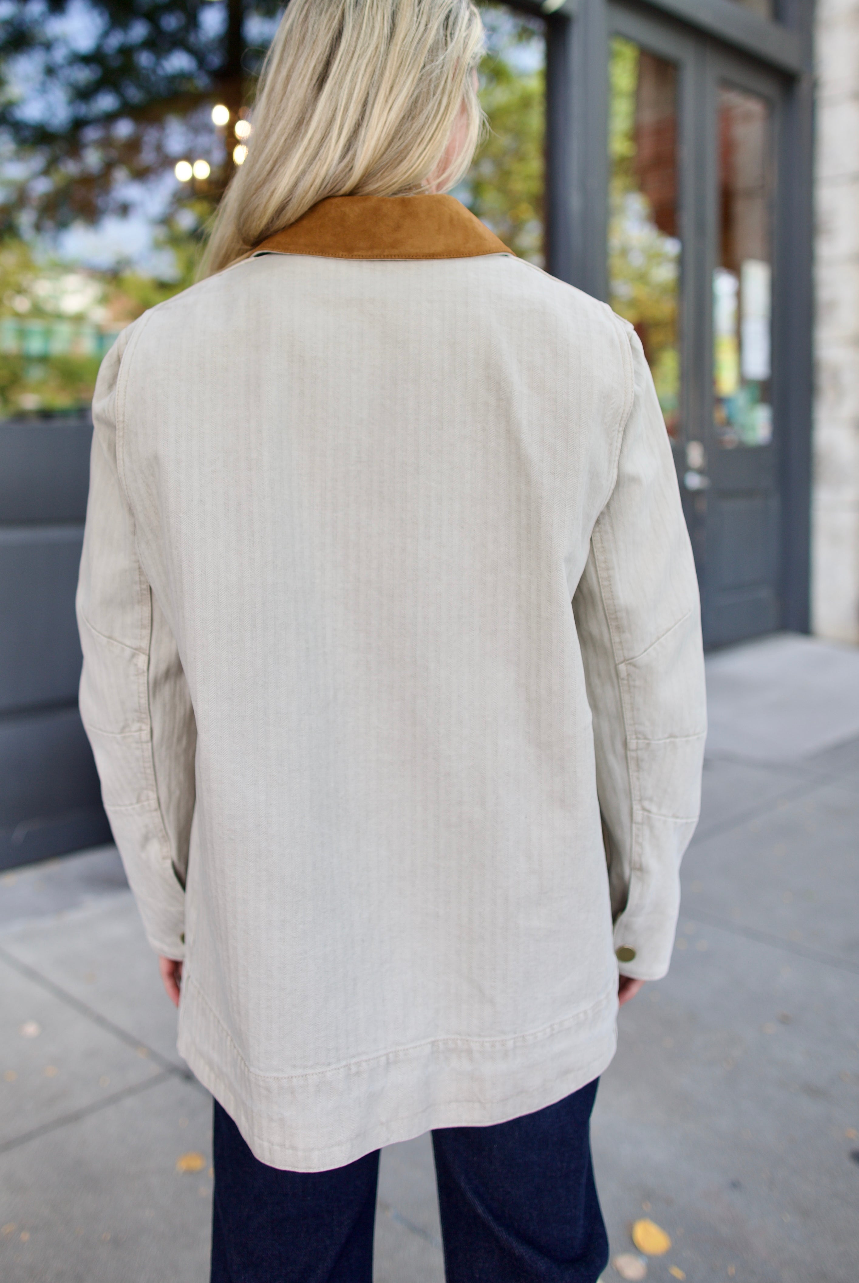 Back of model wearing an elevated casual light weight barn jacket with a suede collar and denim.