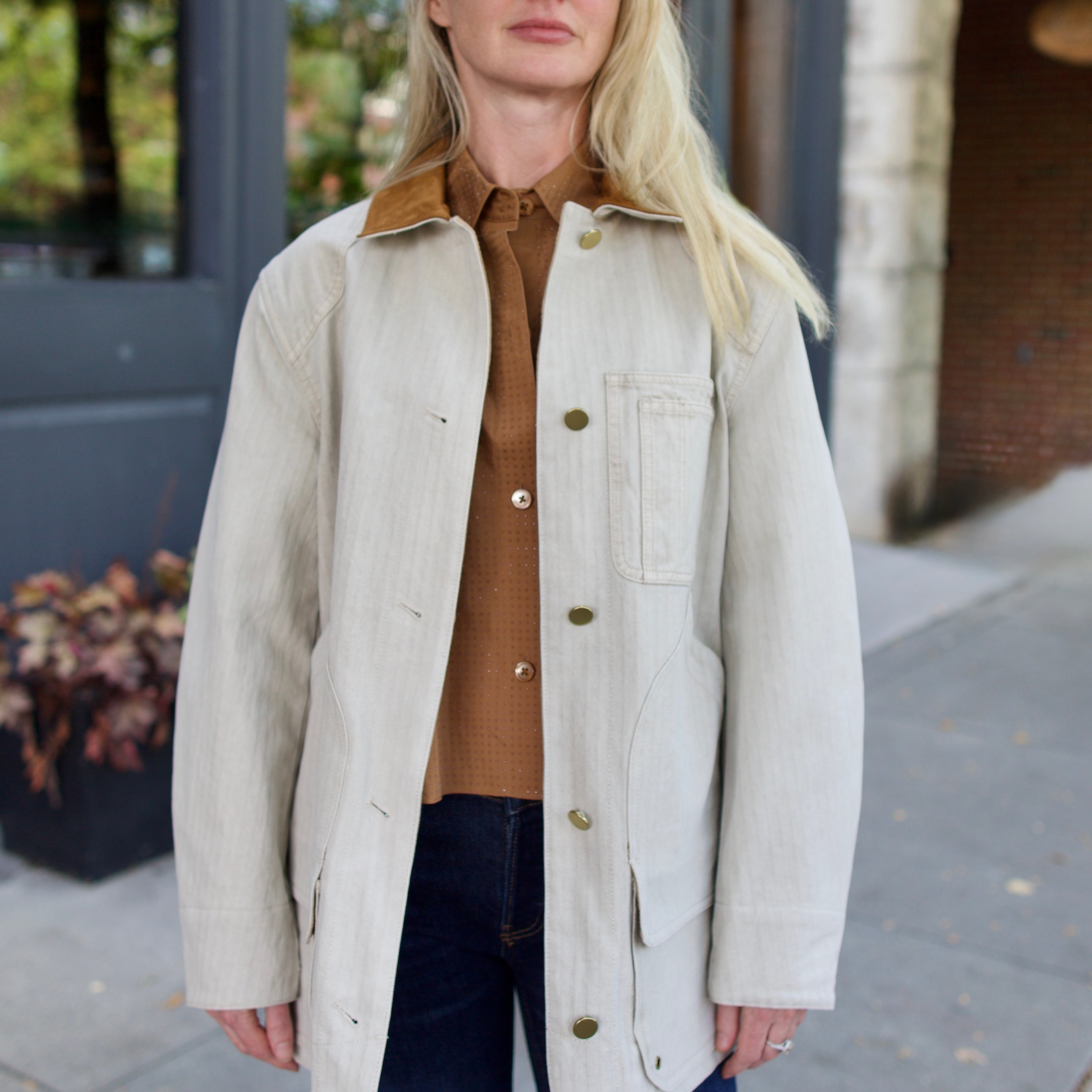 Model wearing a light weight cotton beige barn jacket from Veronica Beard over a TWP brown shirt with blue denim.
