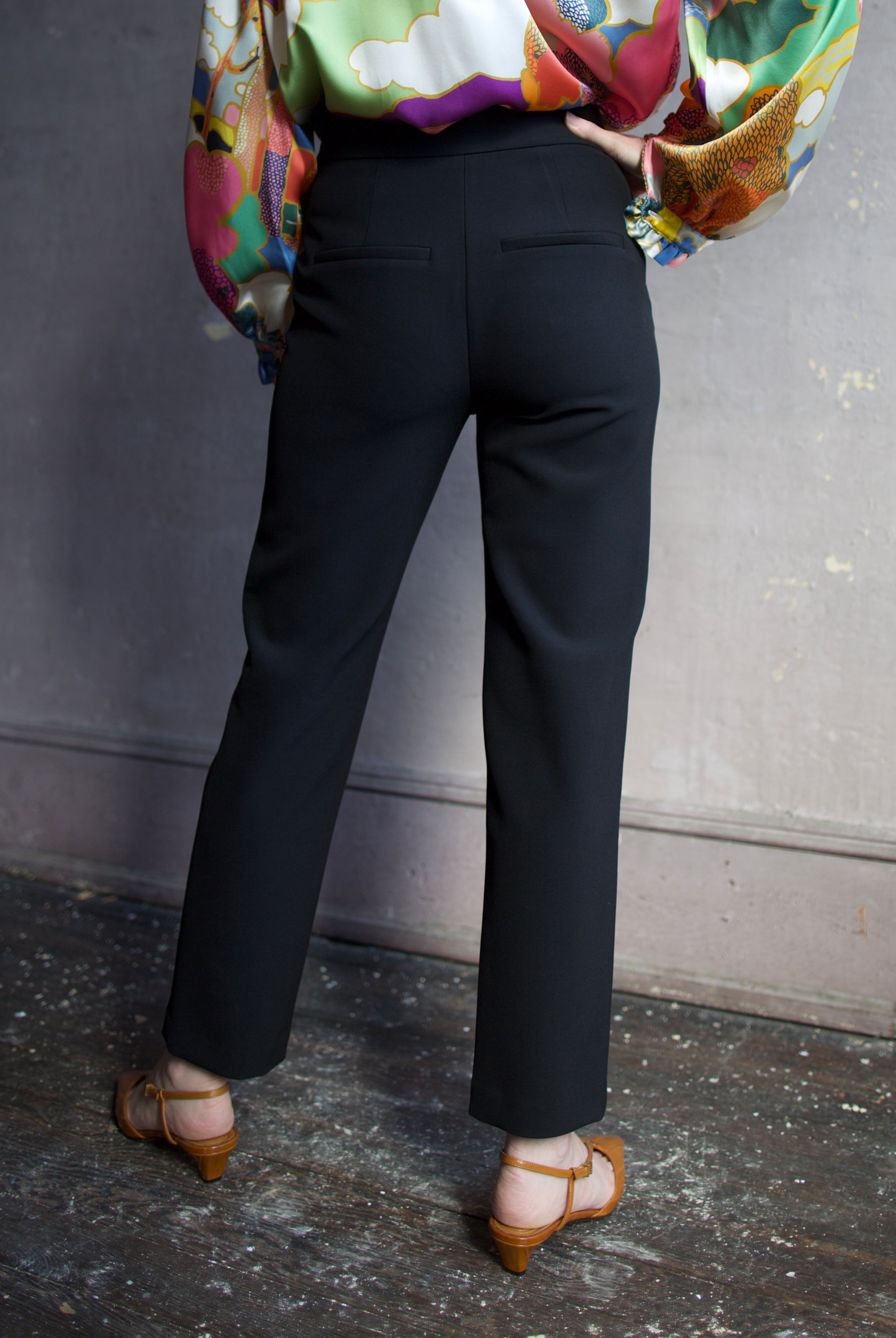 Image featuring a woman wearing the Renzo Pants by Veronica Beard with a tab waistband with a mid rise and straight leg in black with gold finish buttons.