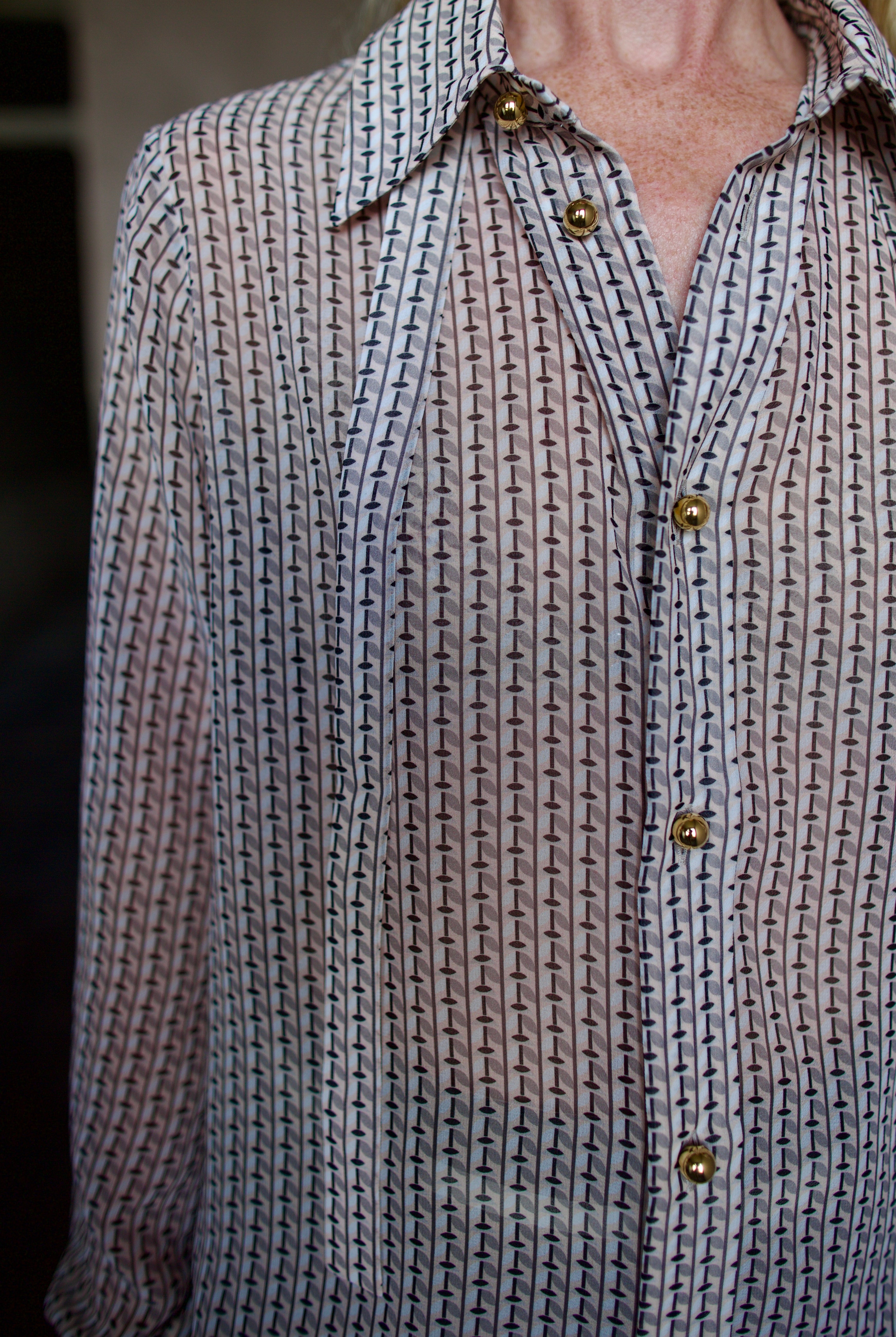 Mature model wearing a sheer geometric shirt with round gold metal buttons by designer WE-AR4