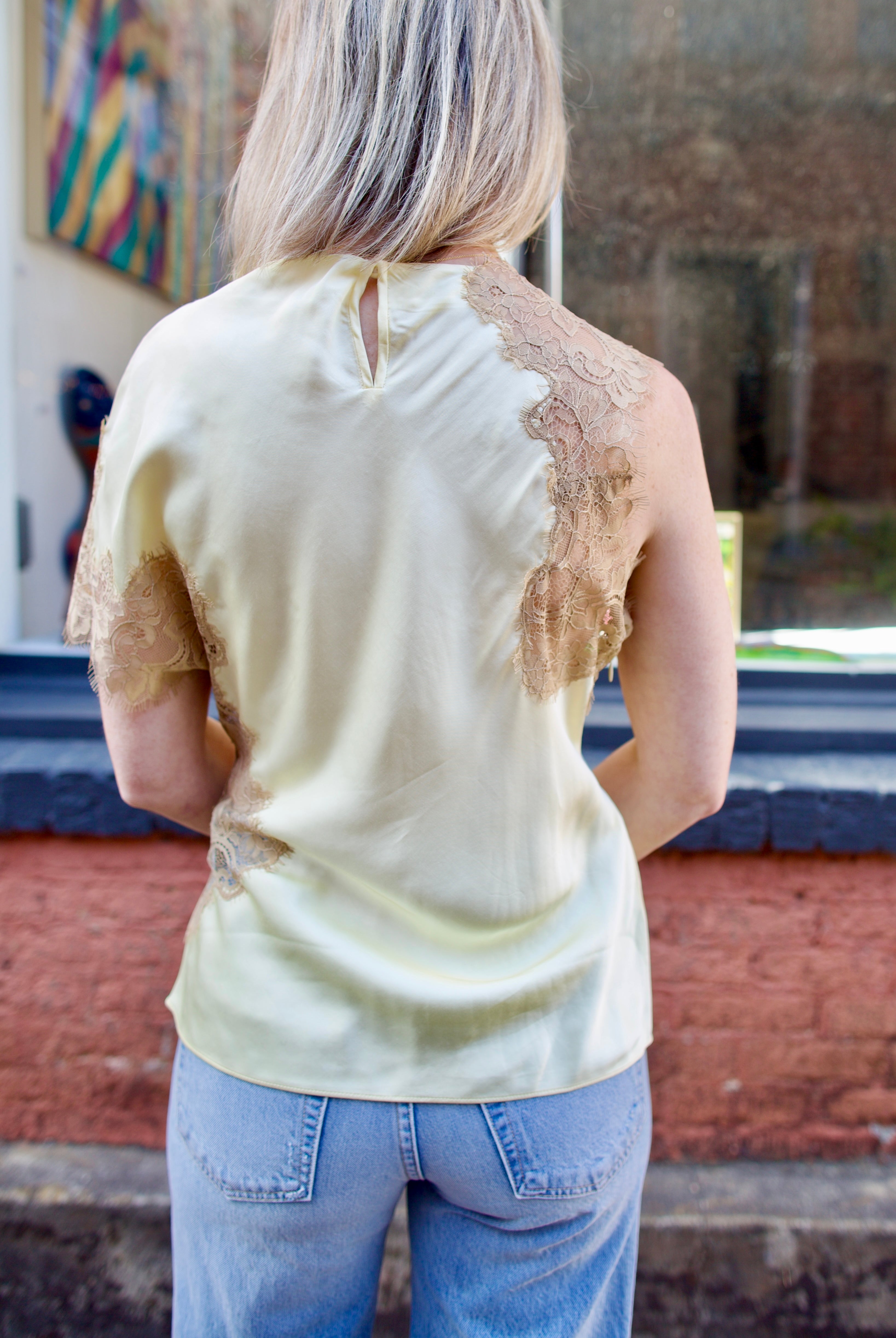 Mature woman wearing the yellow and beige ALC Alessia Top with open neckline, asymmetrical fit and lace detailing