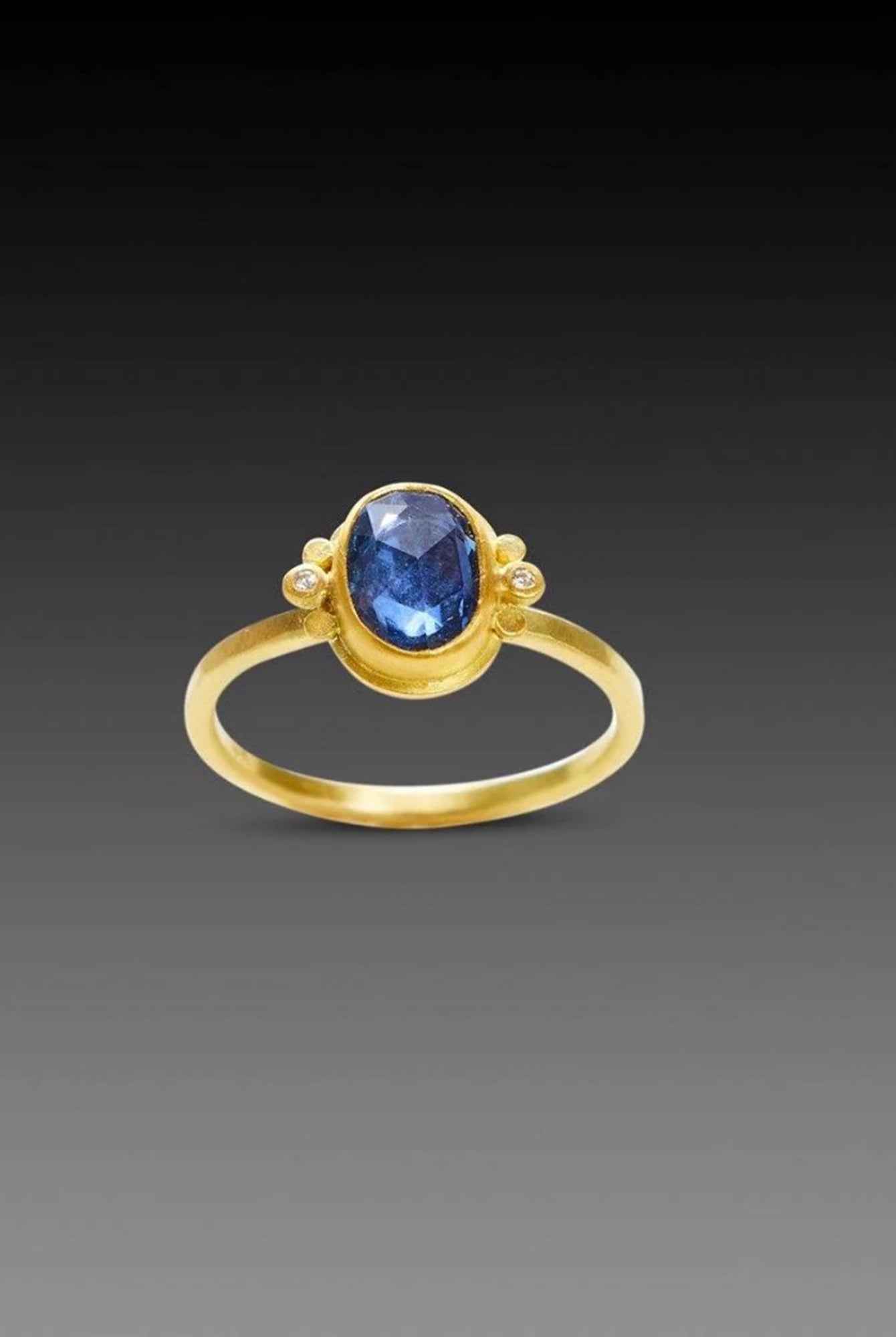 Image of handmade rosecut oval blue sapphire ring by Ananda Khalsa designed with a 22kt gold bezel, 18kt gold band, and 22kt gold diamond trios.