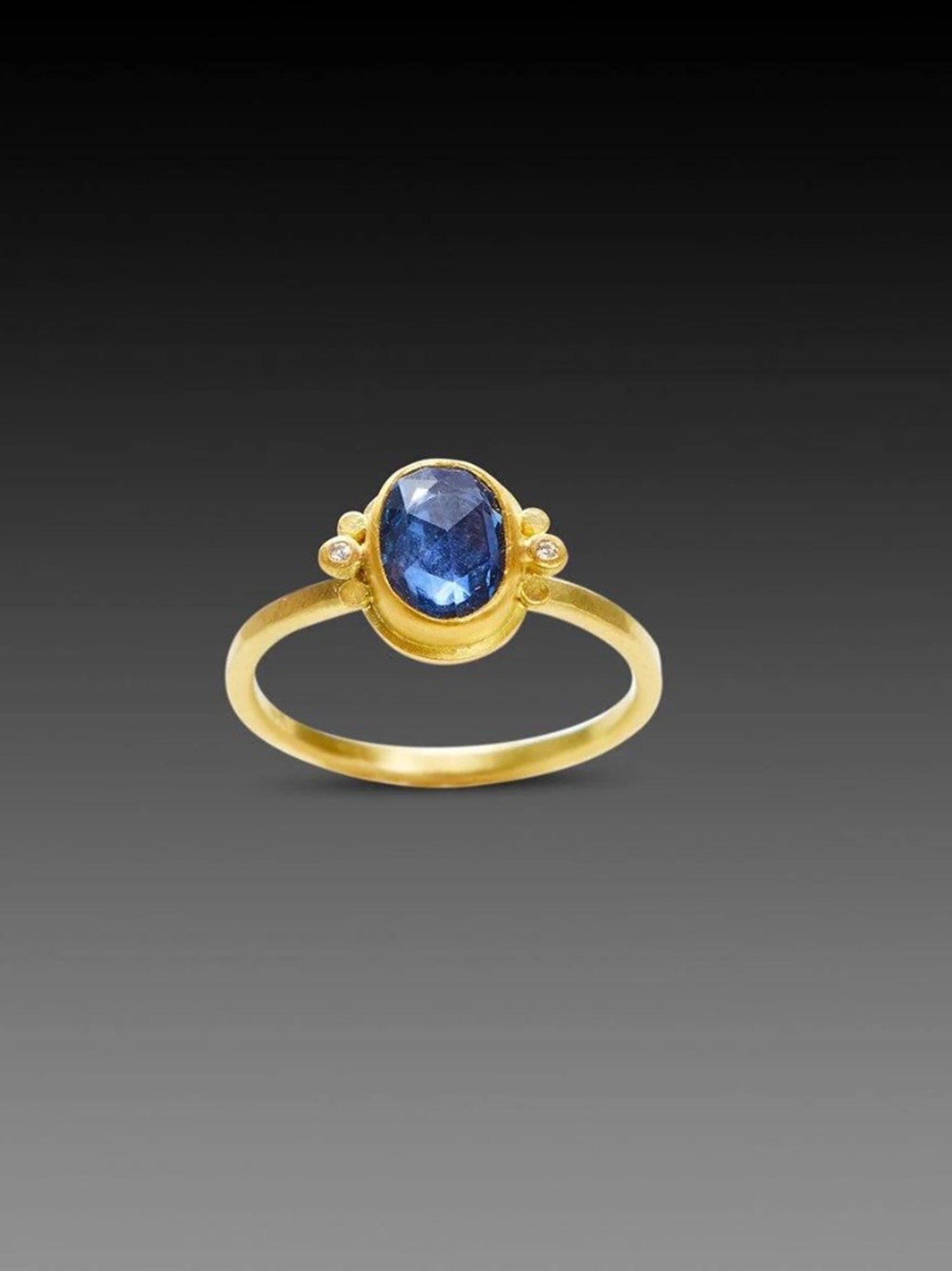 Image of handmade rosecut oval blue sapphire ring by Ananda Khalsa designed with a 22kt gold bezel, 18kt gold band, and 22kt gold diamond trios.