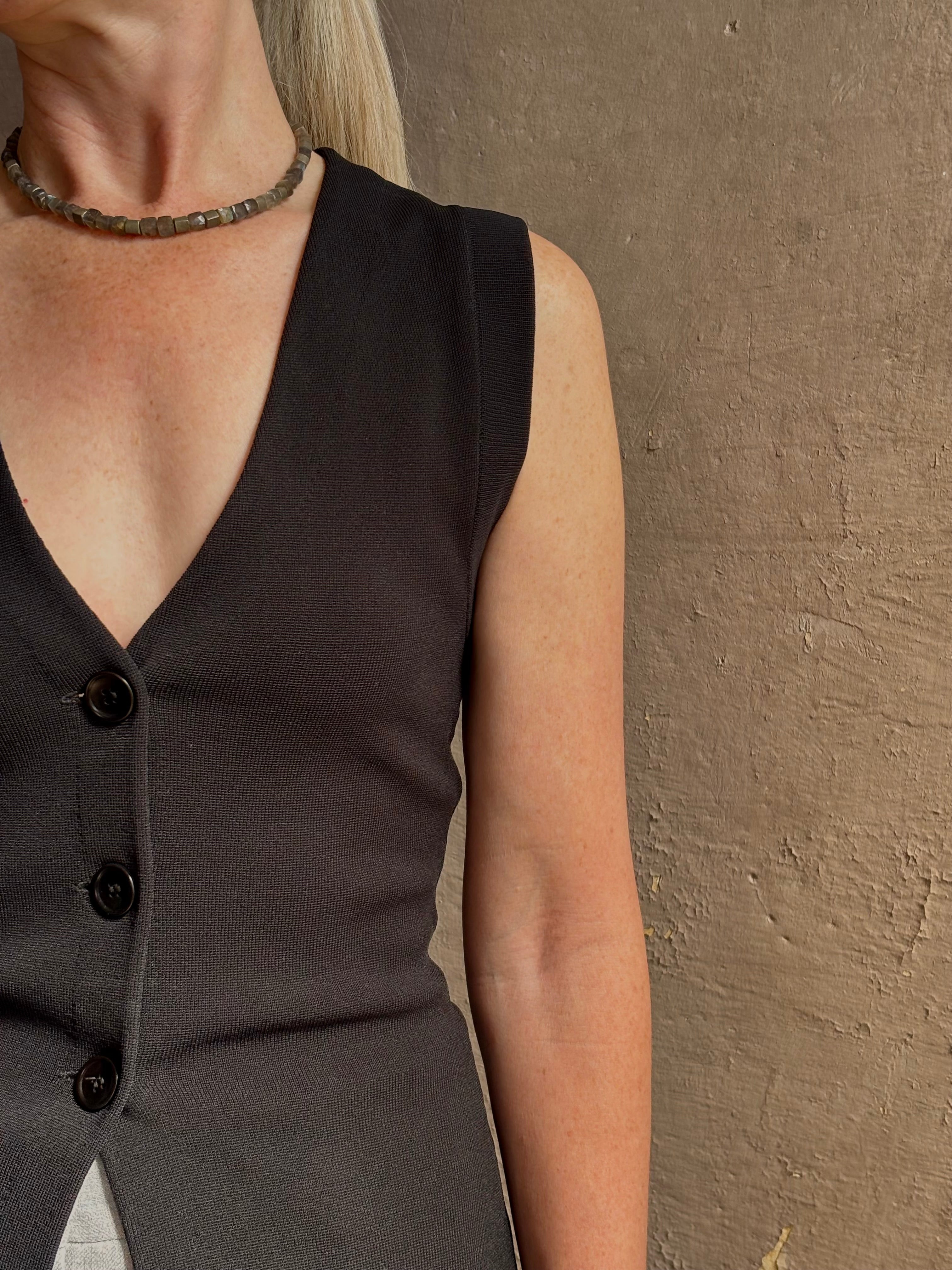 Mature woman wearing a flattering Apiece Apart Marca Knit Top in black with 3 button closure, v- neck and sleeveless